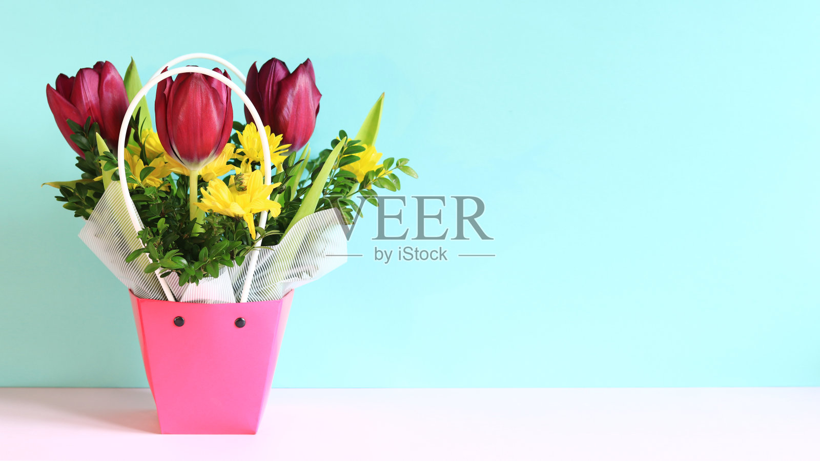 一束春天的花，粉色的篮子里有郁金香。蓝色背景上的春天花朵照片摄影图片