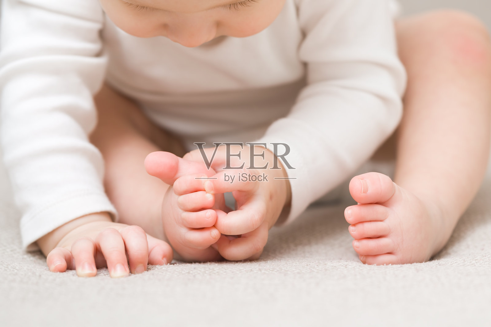 小男孩坐在地毯上。双手触摸，赤脚探索。特写镜头。前视图。9个月大的婴儿发育。照片摄影图片