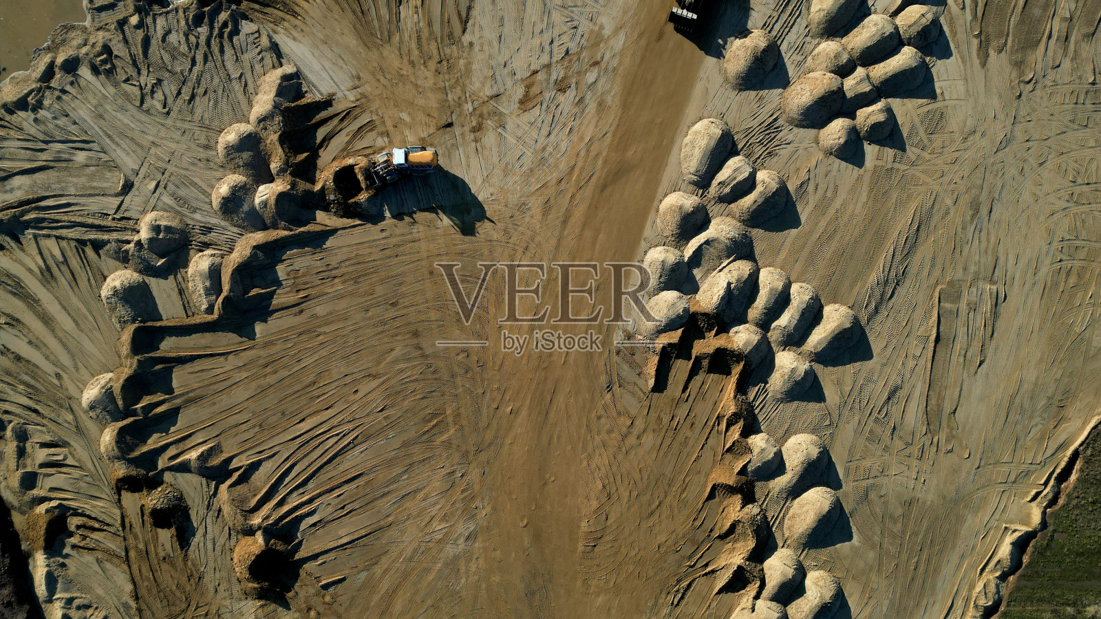 露天砂矿的Arial视图。一个前装载机从桩子里装沙子。在采石场工作的重型采矿机械。大量的车轮痕迹和成堆的沙子就像沙漠的沙丘或乳房，干燥，沙质，沙丘照片摄影图片