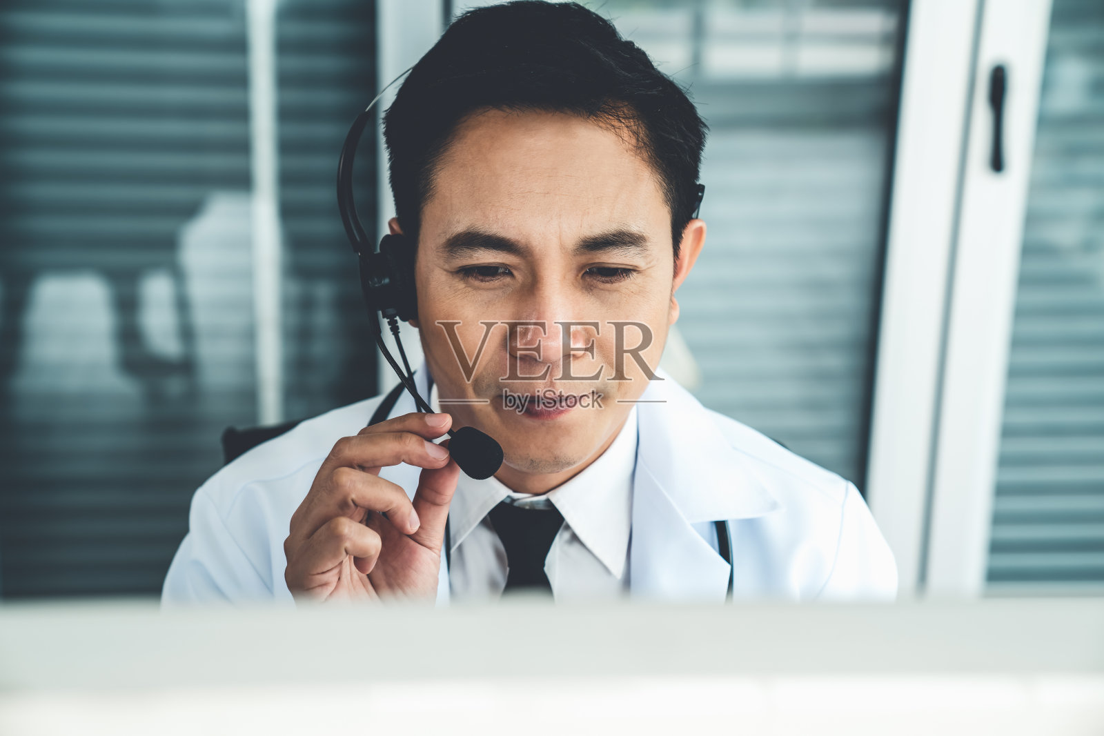 医生戴着耳机在诊所或医院积极视频通话。远程保健和远程医疗服务的概念。照片摄影图片