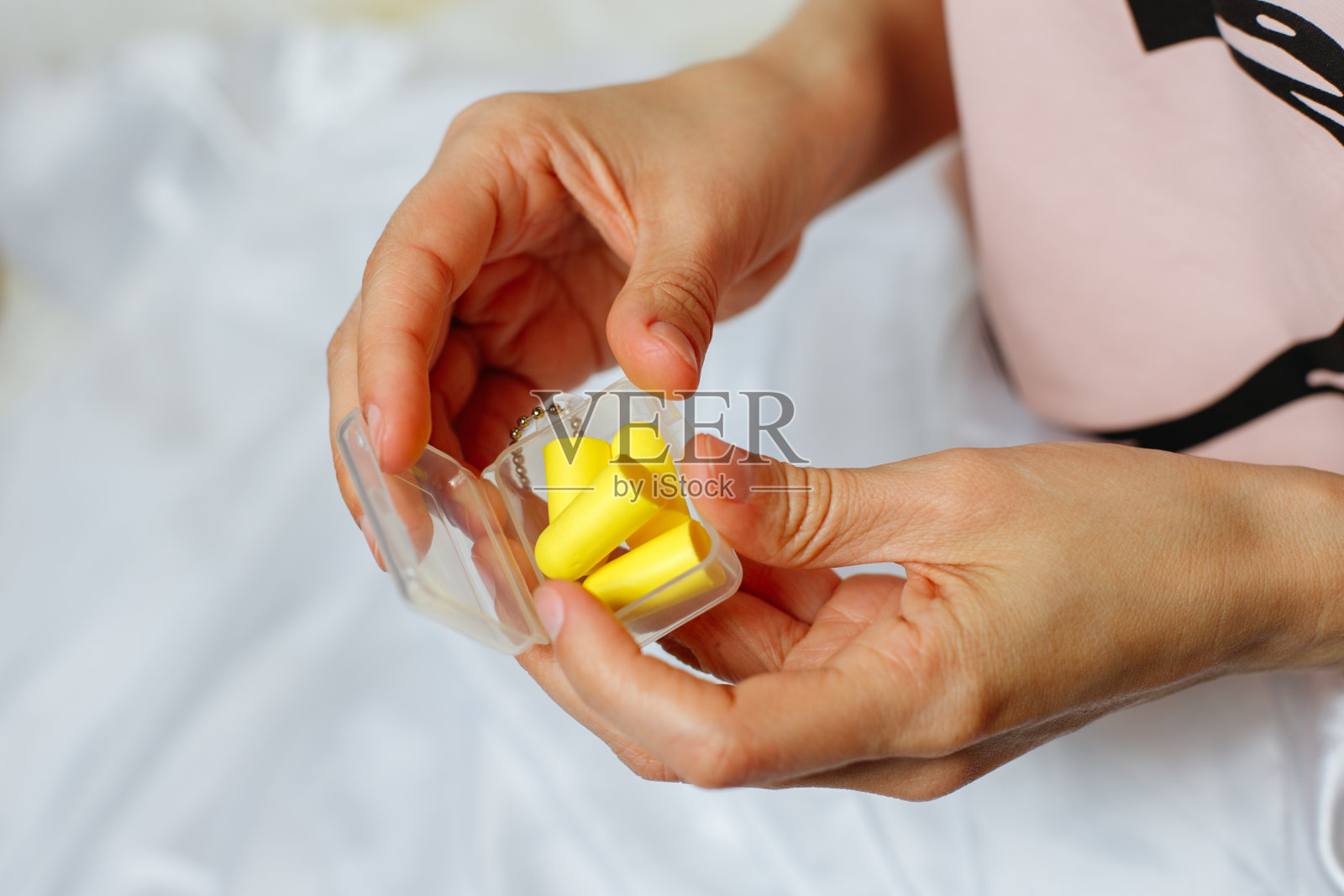 女性手和黄色耳塞的特写。拿着一盒耳塞的女人。粉红色的背景。本空间照片摄影图片