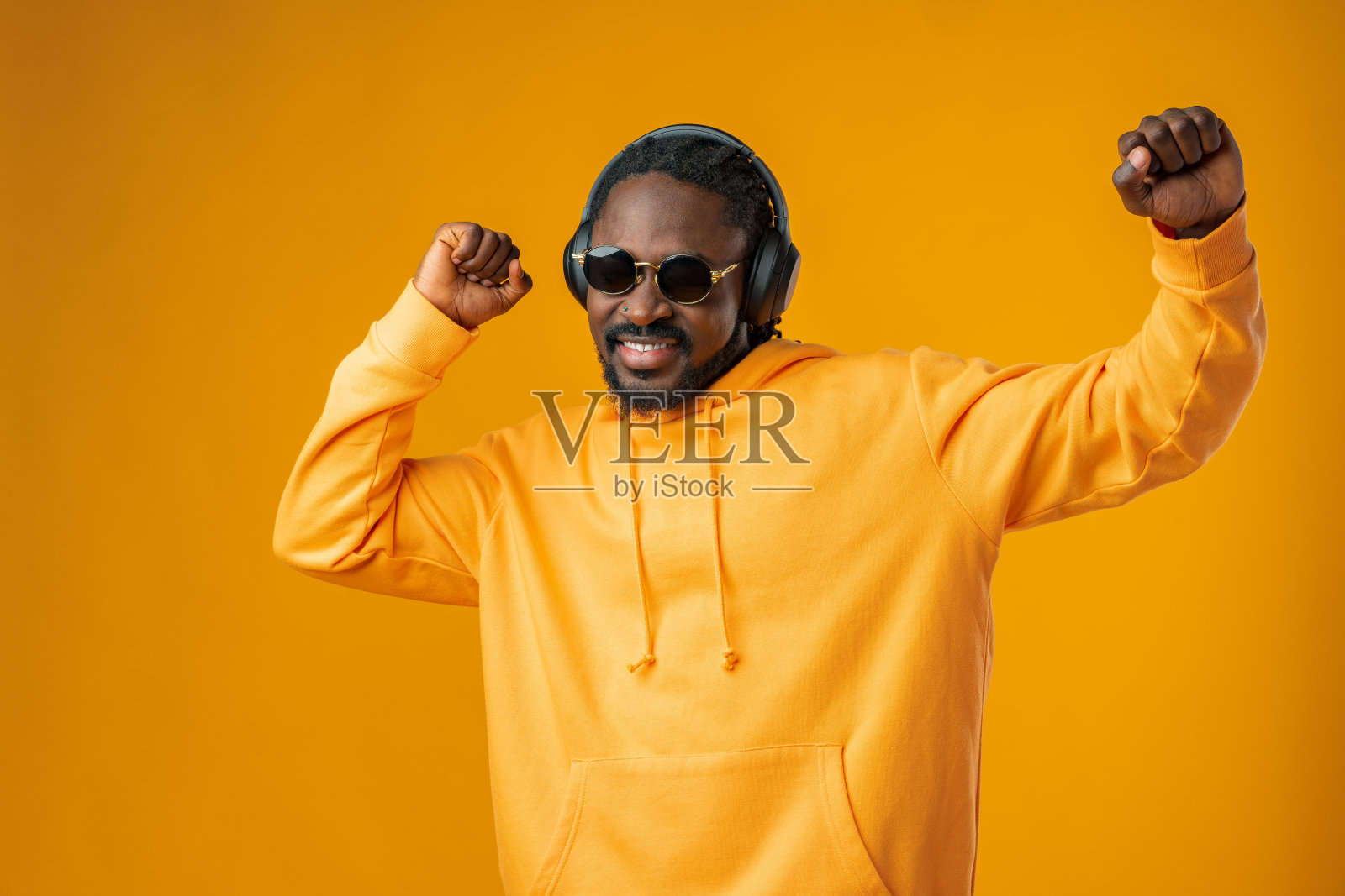 年轻的非洲男子听音乐与耳机隔离在黄色背景。照片摄影图片