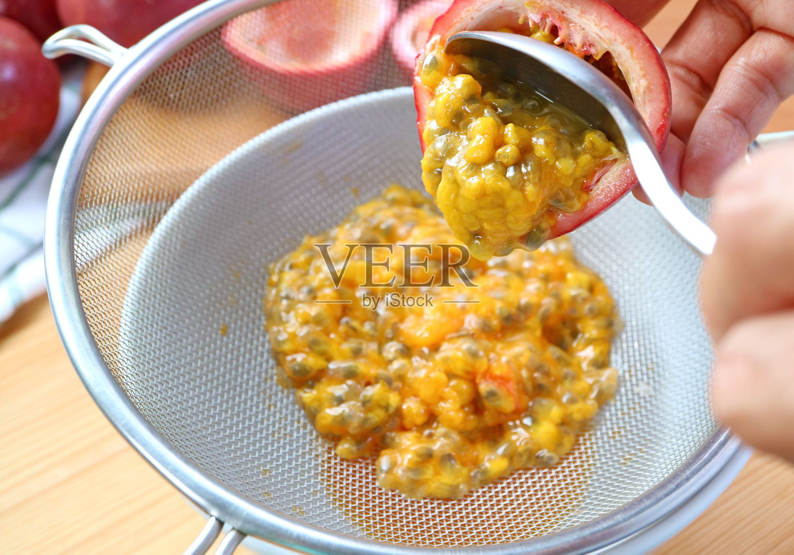 用勺子将百香果果肉舀入滤网，从果肉中提取液体，制成果泥照片摄影图片
