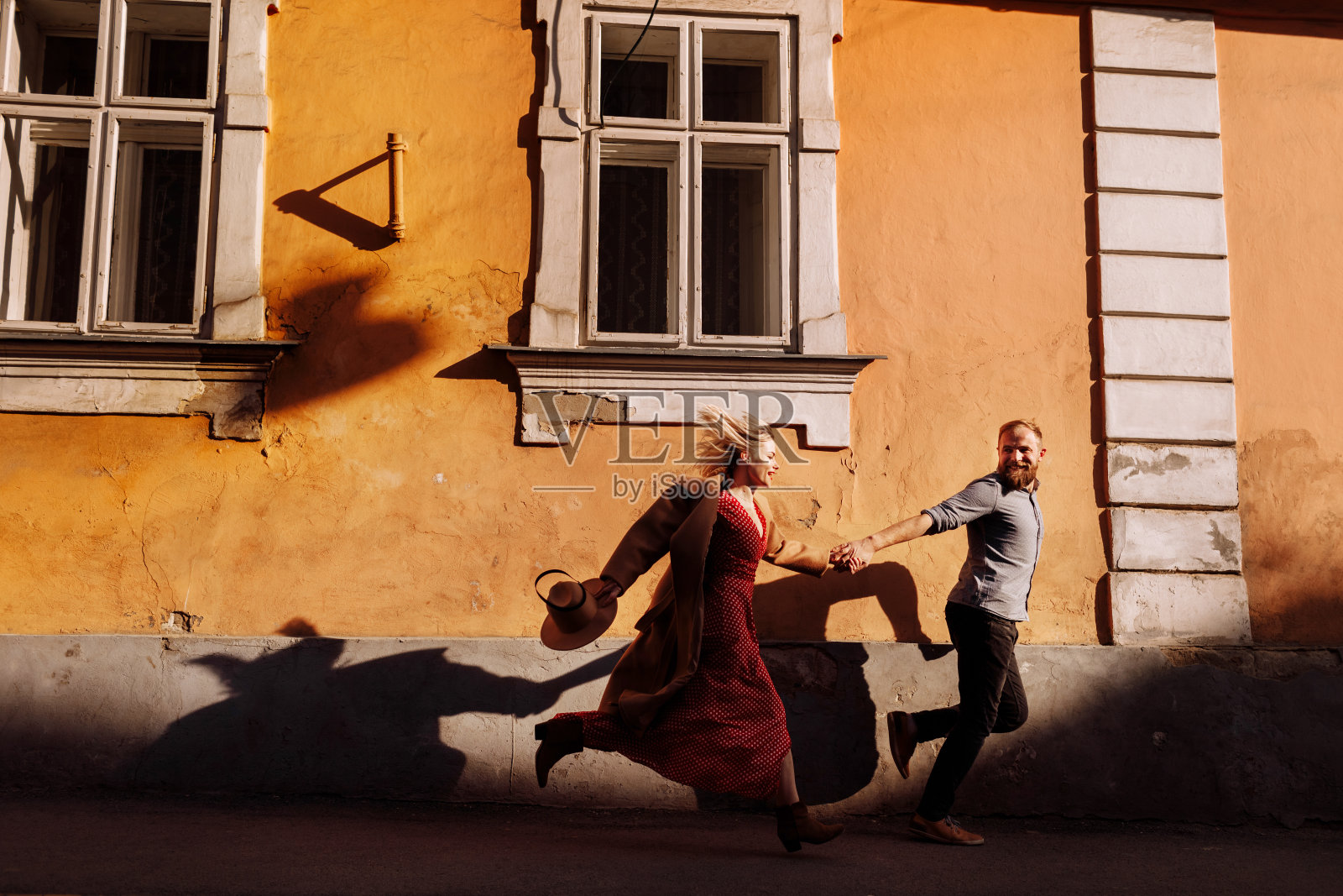 时尚开朗的年轻潮人大胡子男人和金发女人手牵着手在古老的欧洲城市街道上玩耍。幸福的情侣在情人节跑步和浪漫的约会。照片摄影图片