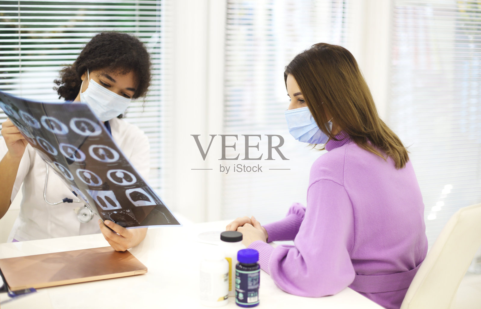 戴着口罩的非裔美国女医生向妇女解释x光扫描结果照片摄影图片