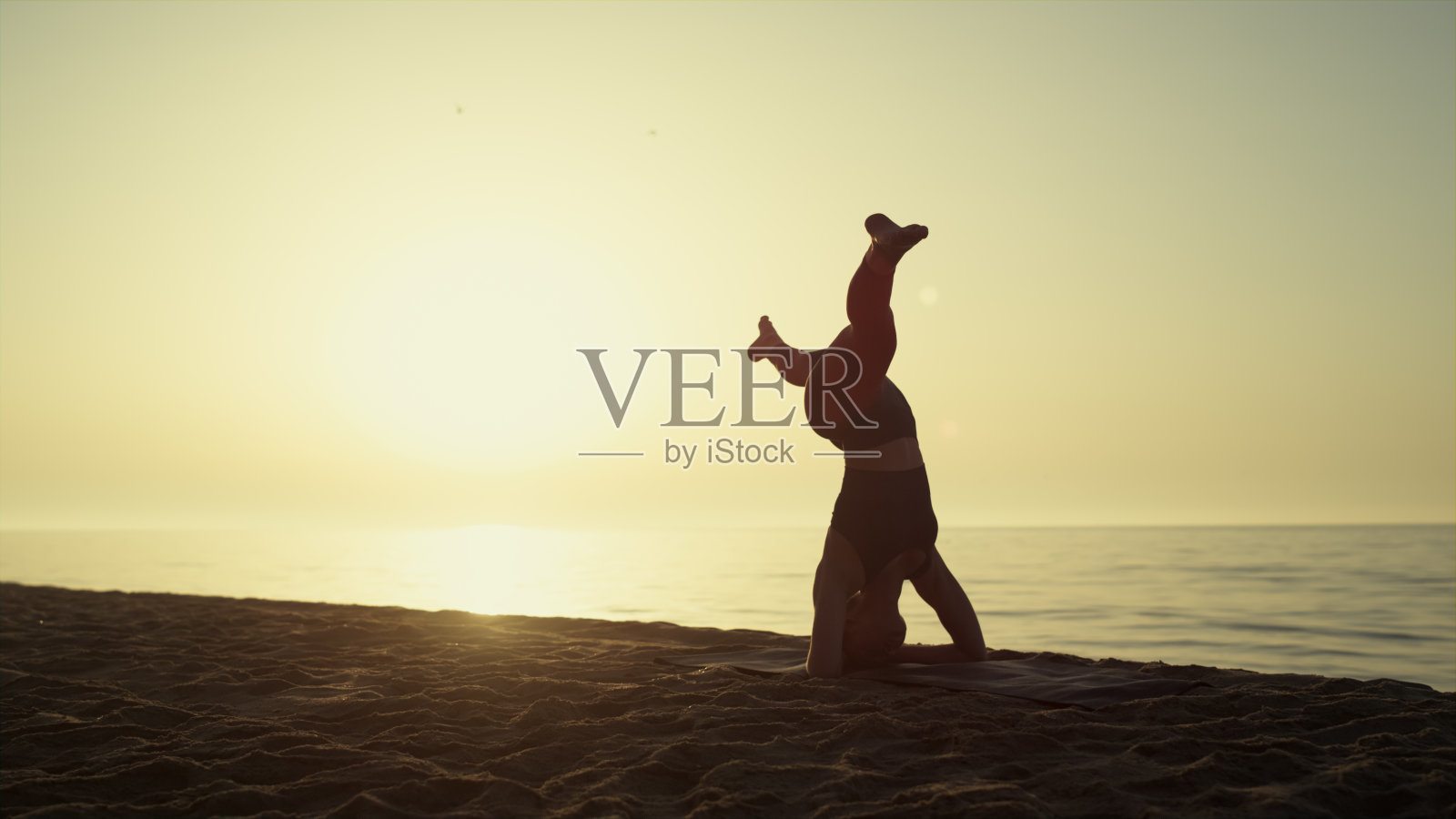 瑜伽女人在日落倒立。强壮的女孩倒立着。照片摄影图片