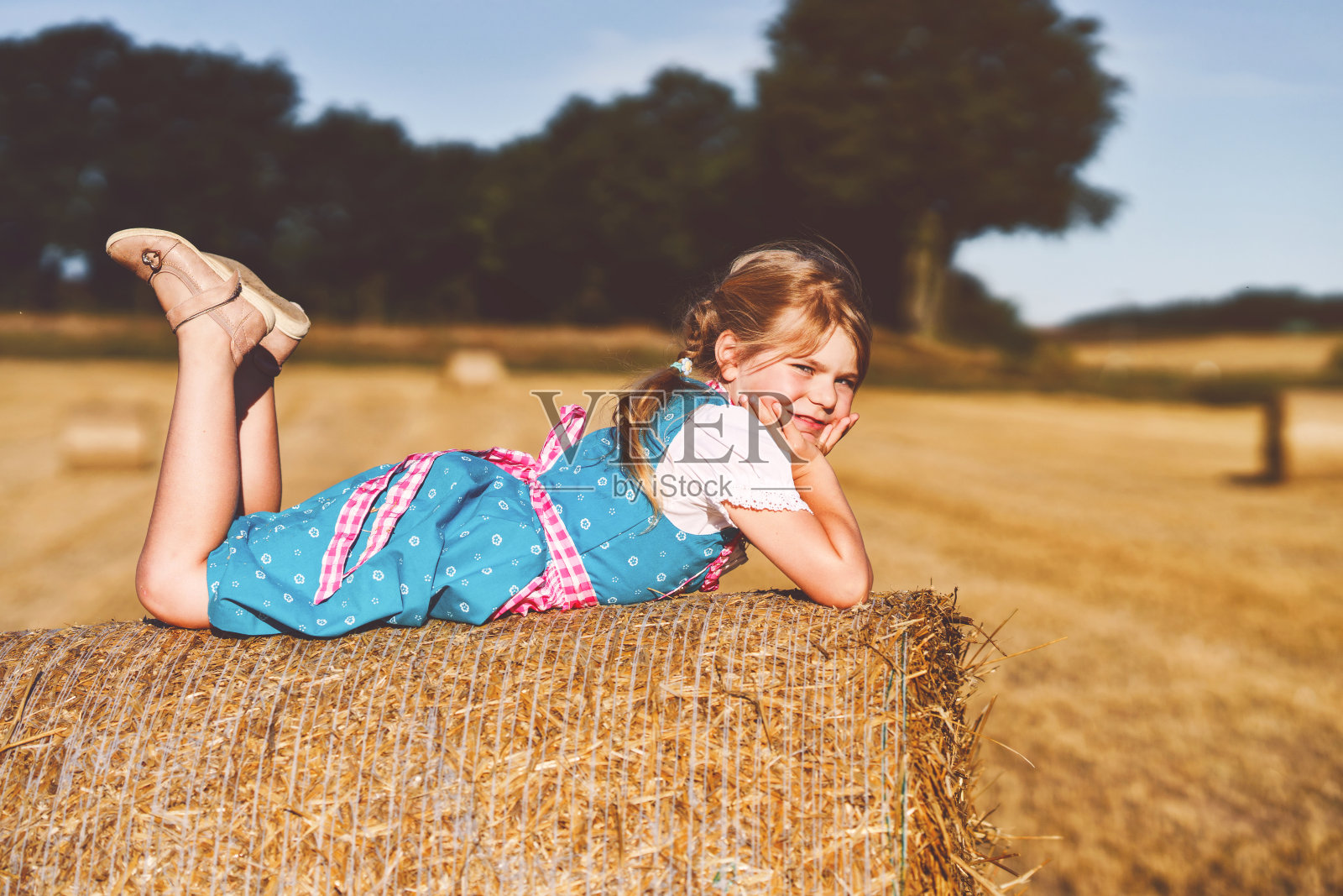 可爱的小女孩在传统的巴伐利亚服装在麦田。慕尼黑啤酒节期间，快乐的孩子拿着干草堆。德国夏季收获季节，学前班的女孩在干草堆上玩耍。照片摄影图片