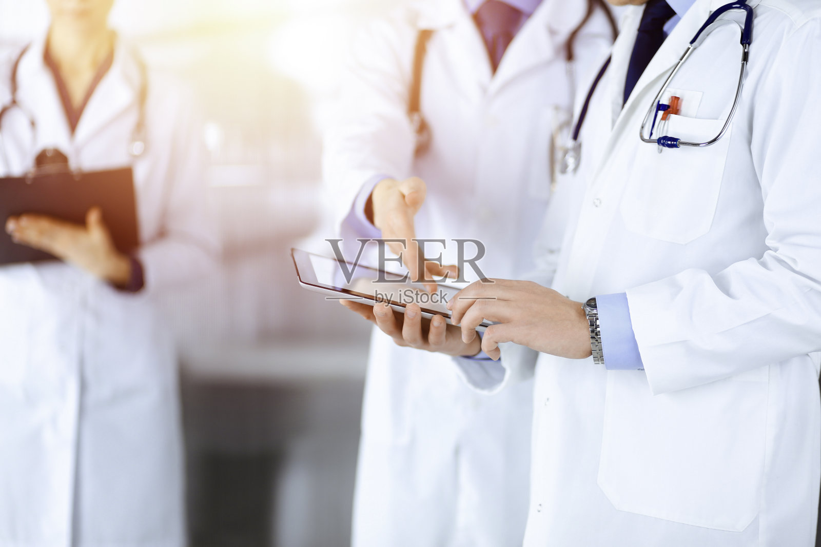 一群不知名的医生站在阳光明媚的医院办公室里，用平板电脑查看一些医名记录。医生随时准备检查和帮助病人。医疗帮助医疗保险照片摄影图片