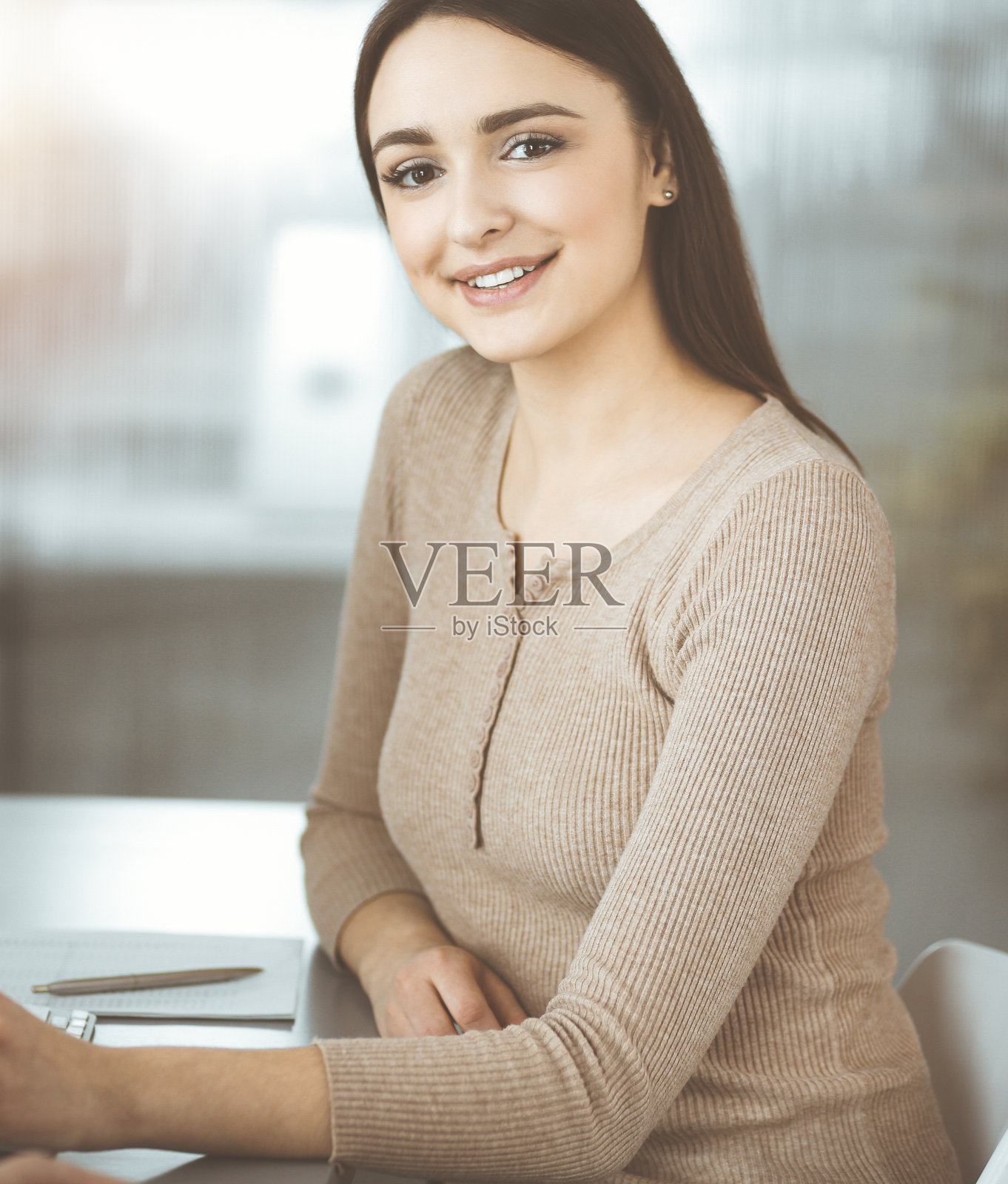 在阳光明媚的办公室里，年轻的商务人士坐在办公桌前互相交谈。一位女商人正在向她的同事解释什么照片摄影图片