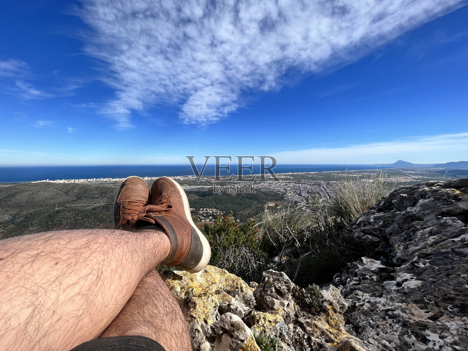 一名年轻的徒步旅行者在爬山后，坐在山顶上，看到包括地中海在内的所有风景。照片摄影图片