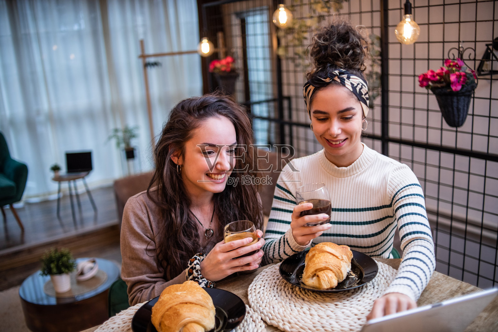 两个女人，朋友，坐在家里的酒吧里，吃早餐，喝咖啡，用平板电脑上网照片摄影图片