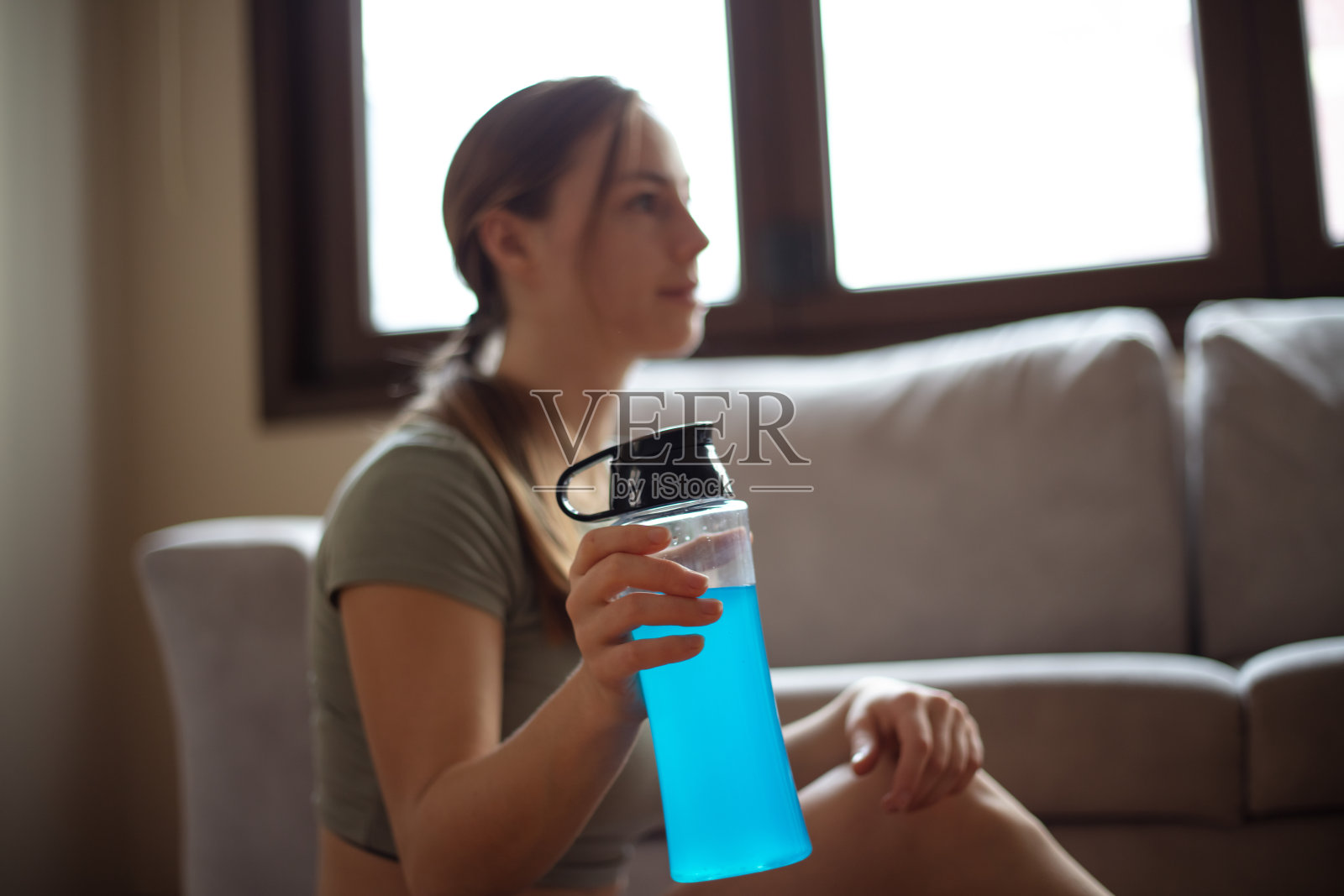 年轻女子在家里的客厅锻炼期间补水。照片摄影图片