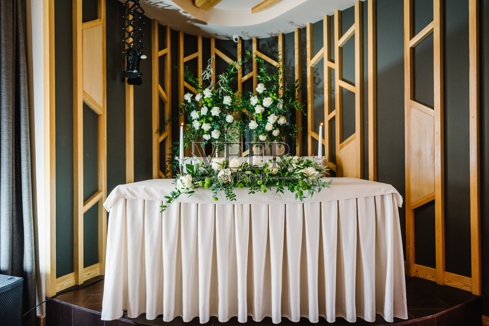 喜庆的餐桌以桌布近拱，以鲜花和绿色植物装饰，在宴会厅蜡烛。新婚夫妇在宴会区用餐。婚礼的设置。照片摄影图片