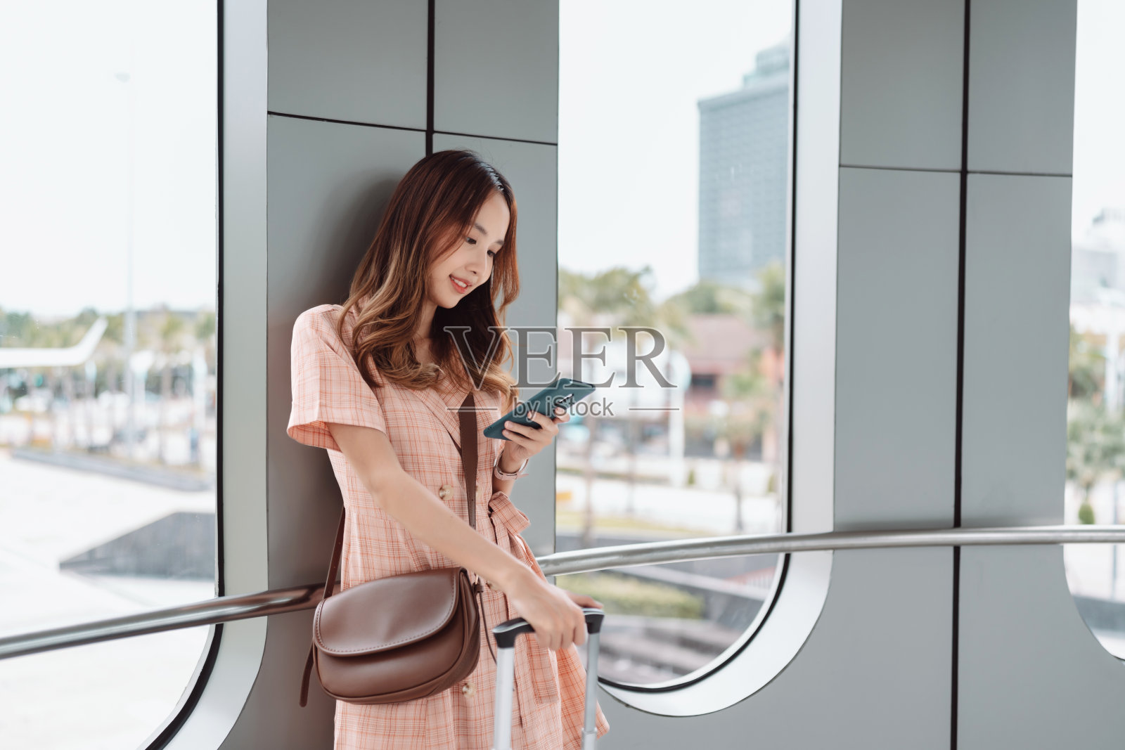 亚洲女性青少年在机场航站楼使用智能手机，带着行李箱和背包，在假期、夏天旅行，放松等待航班运输，在线办理登机手续或预订机票照片摄影图片