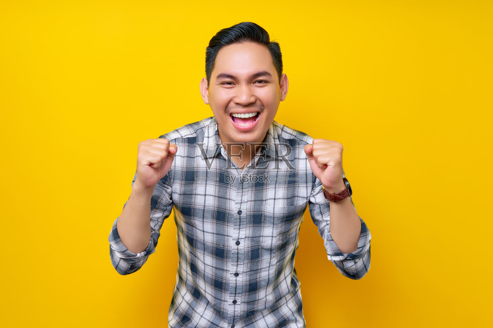 兴奋的年轻英俊的亚洲男子庆祝胜利或成功，举起拳头孤立在黄色背景。人的生活方式概念照片摄影图片