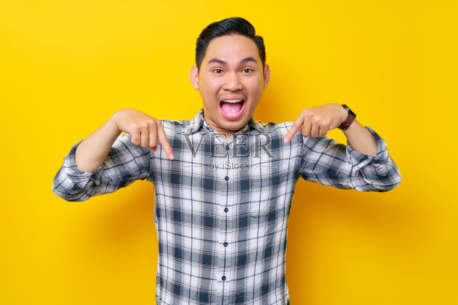 兴奋的年轻英俊的亚洲男子穿着格子衬衫指向下，显示广告隔离在黄色背景上的自由位置。人的生活方式概念照片摄影图片