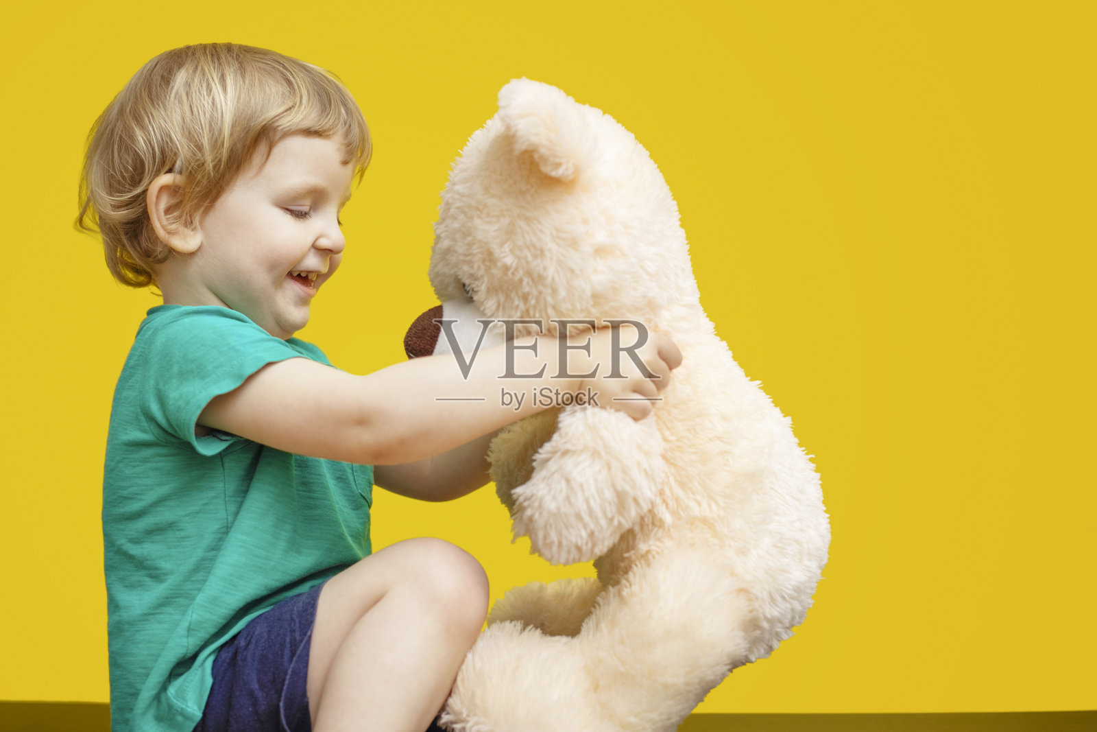 小男孩抱着黄色背景的泰迪熊玩具照片摄影图片