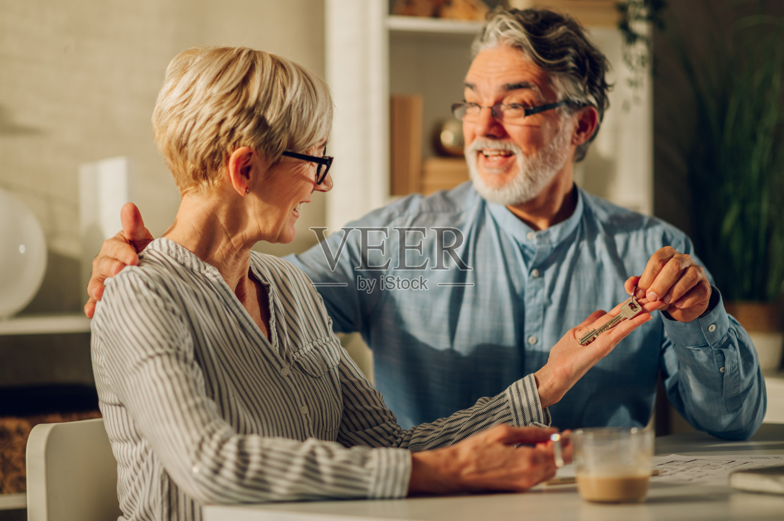 老夫妇坐在桌旁，拿着他们新家的钥匙照片摄影图片
