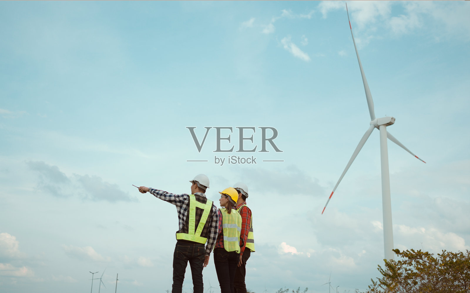 三位工程师讨论并检查风力涡轮机领域进展的后视图。照片摄影图片