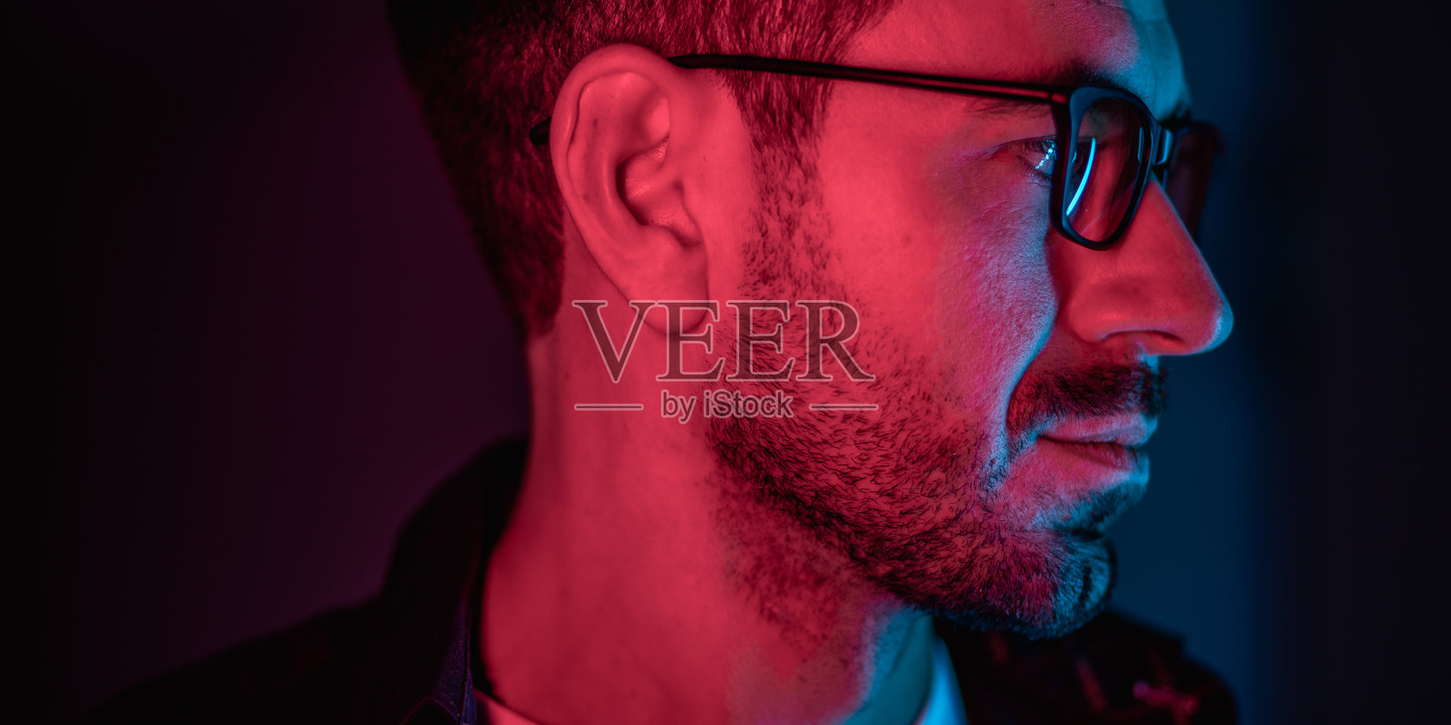 男人的男性肖像与霓虹灯。红色，蓝色，紫色和洋红色与深色背景。人在室内戴眼镜，穿深色夹克和白色t恤。未来生活方式概念多色灯照片摄影图片