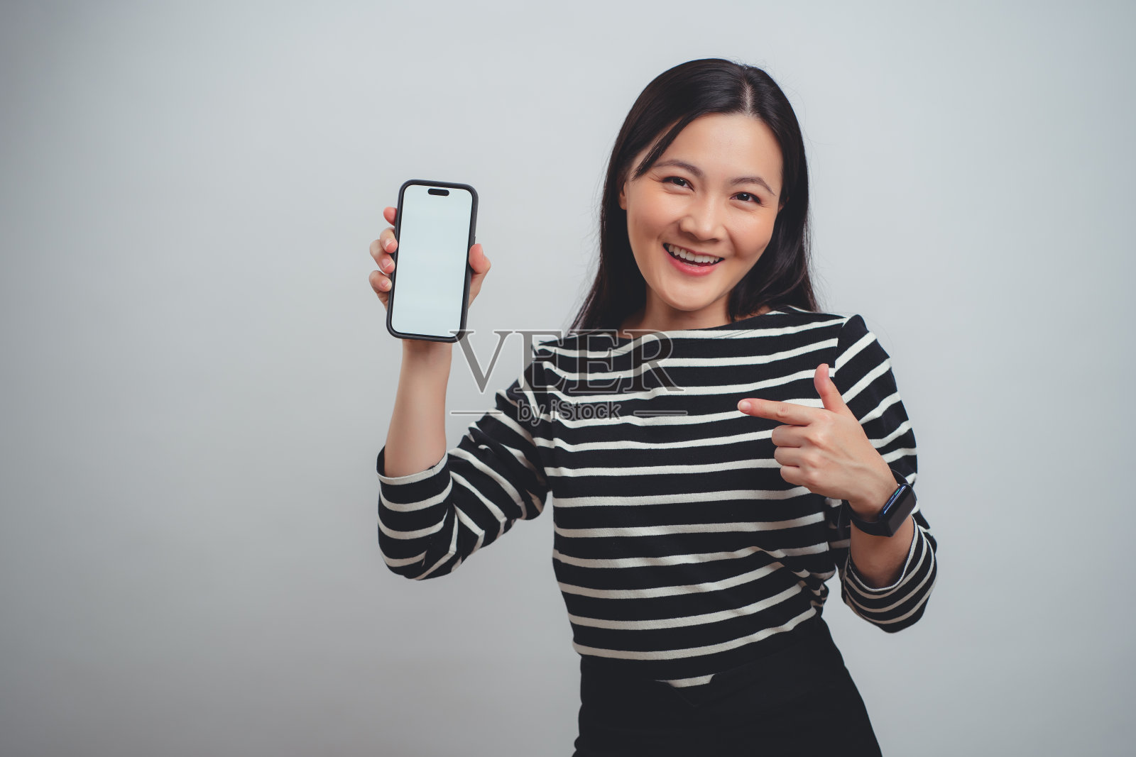 一名亚洲女性开心地笑着，智能手机上的白色屏幕孤立地站在白色背景上。照片摄影图片