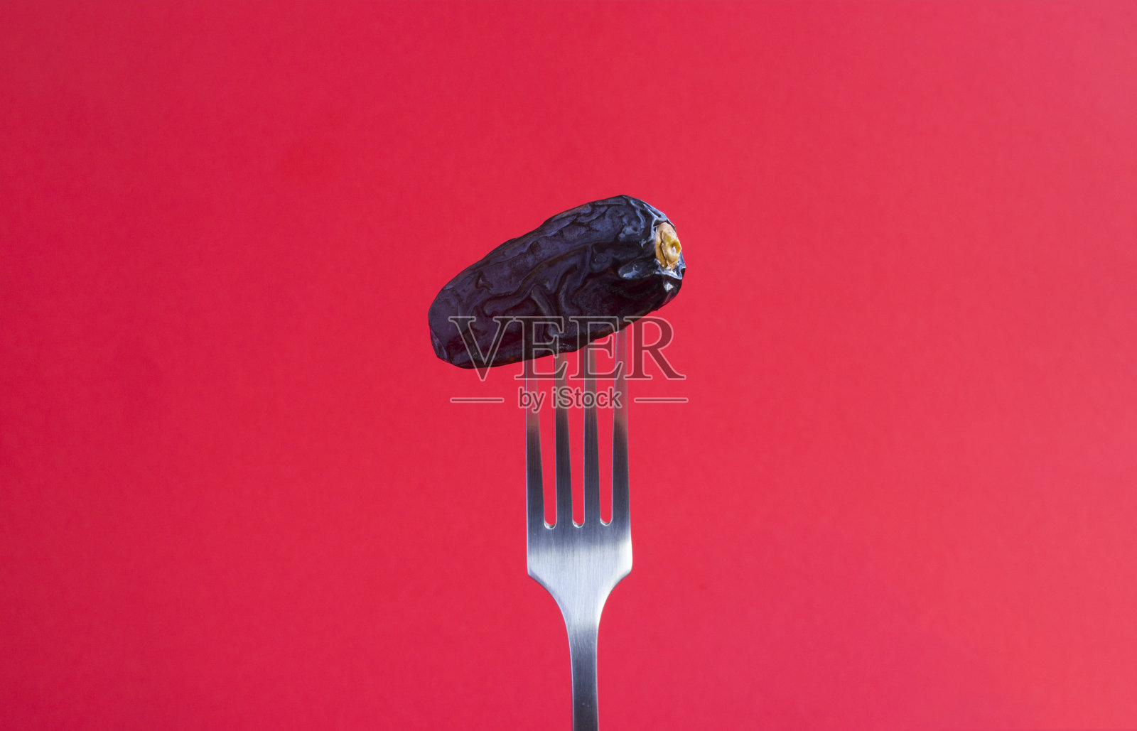 枣子插在红色背景的银叉上。特写镜头。副本的空间。照片摄影图片