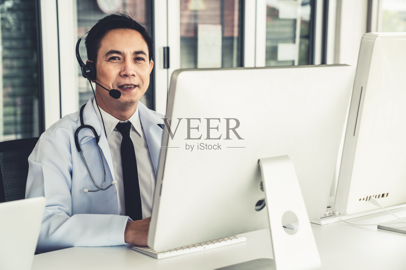 医生戴着耳机在诊所或医院积极视频通话。远程保健和远程医疗服务的概念。照片摄影图片