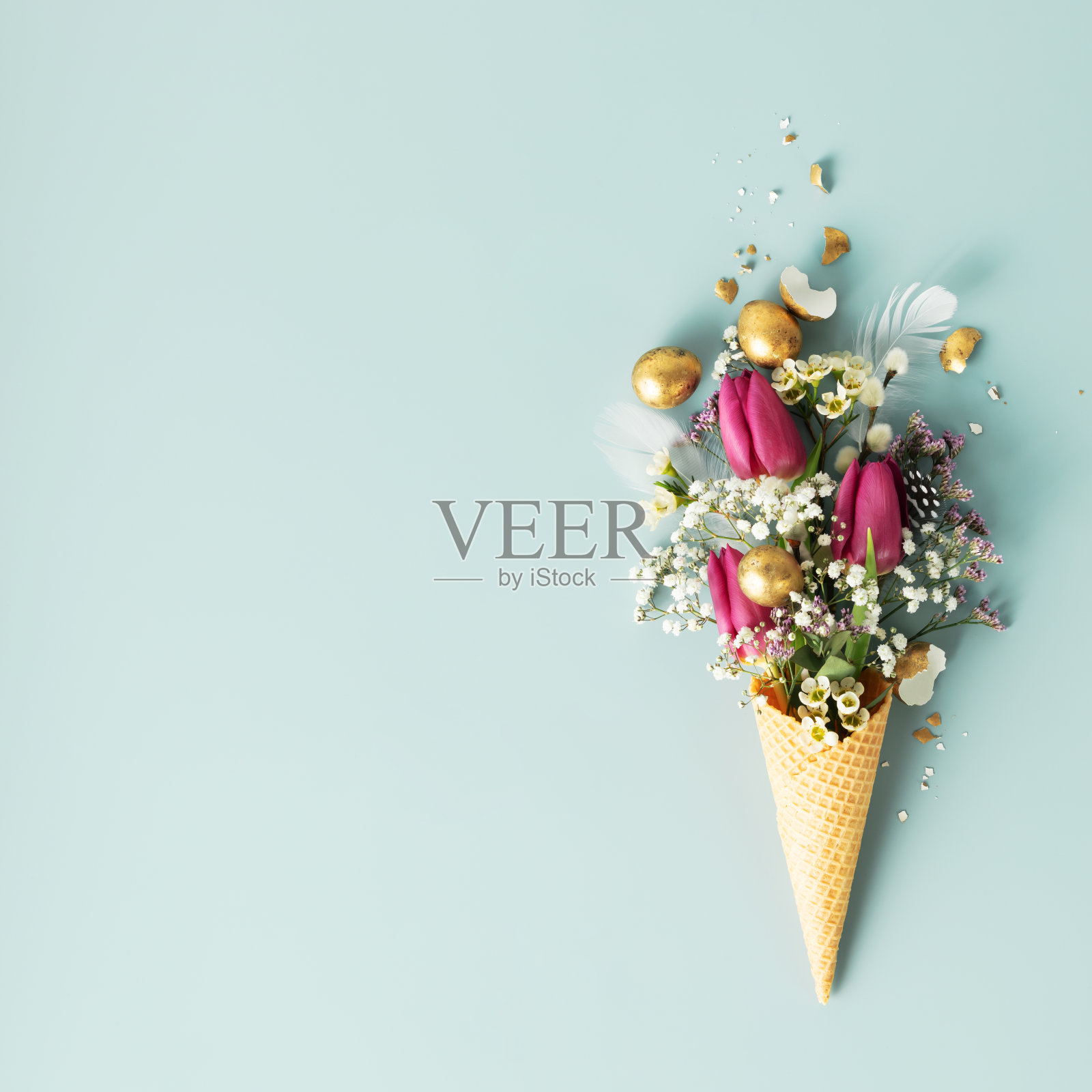 蓝色背景上有美丽的花朵和金色复活节彩蛋的冰淇淋蛋筒照片摄影图片
