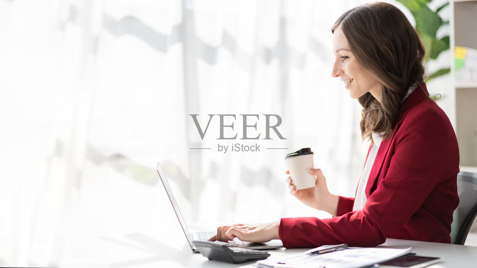 美国女商人自信地微笑着使用笔记本电脑进行财务统计工作，用图表文件演示女会计在办公室分析数据，看着相机照片摄影图片