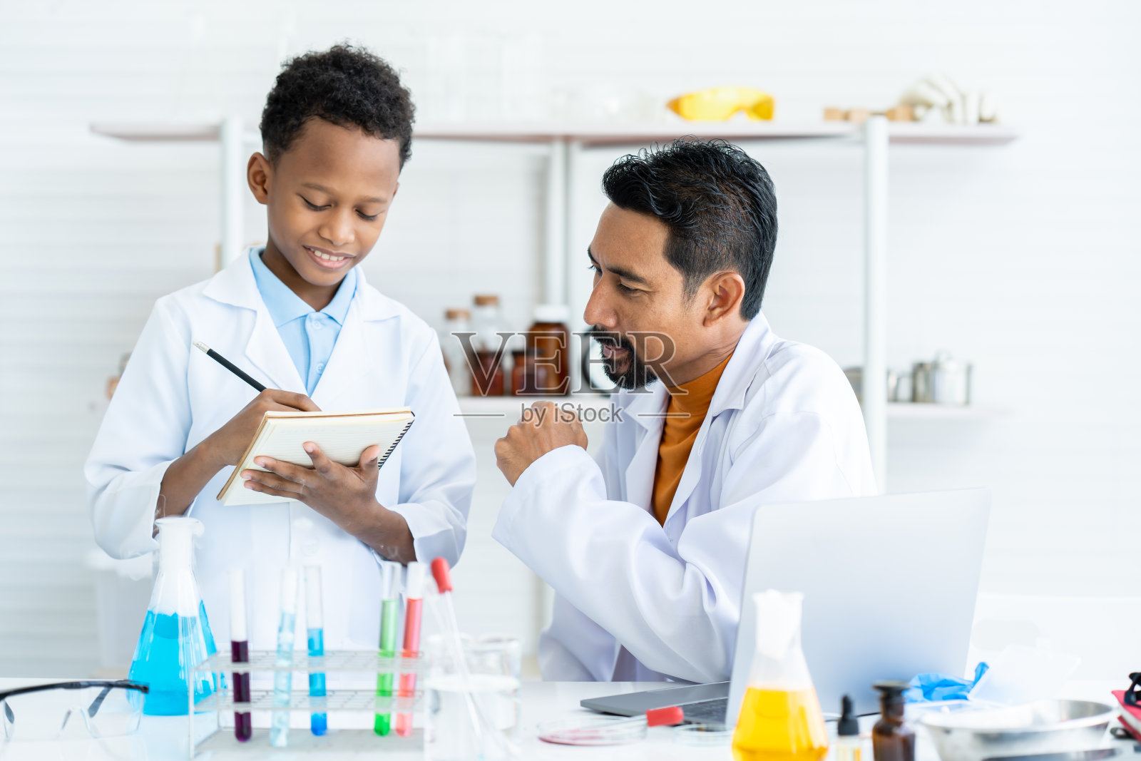 理科老师，教男生，关于化学实验的结果做笔记，在理科科目上，准备让学生行动起来，把纸写下来看看，检查自己是否正确。照片摄影图片