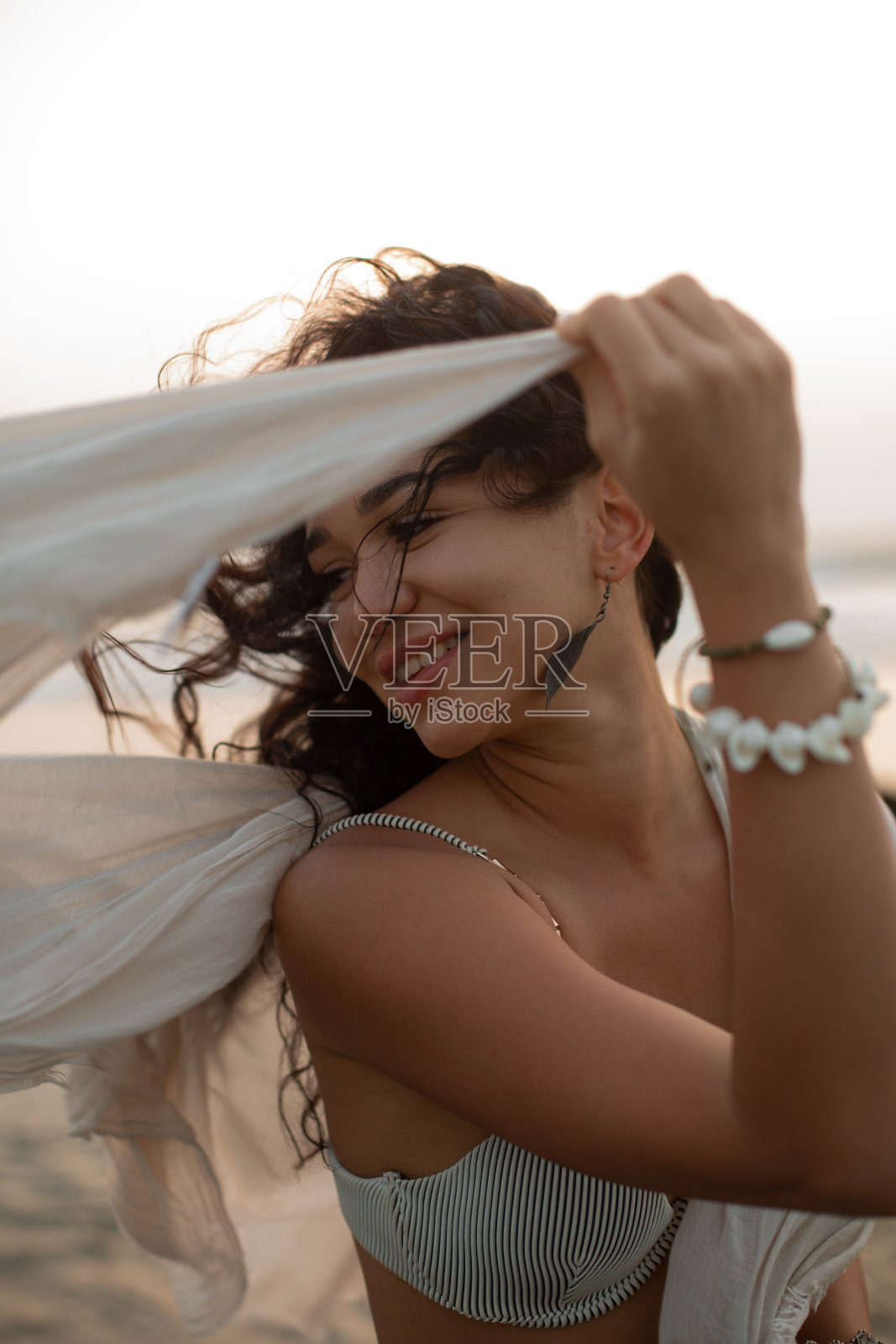 微笑着晒黑的年轻女子沐浴后湿头发享受微风在海滨。日落在ea。好玩的心情。照片摄影图片