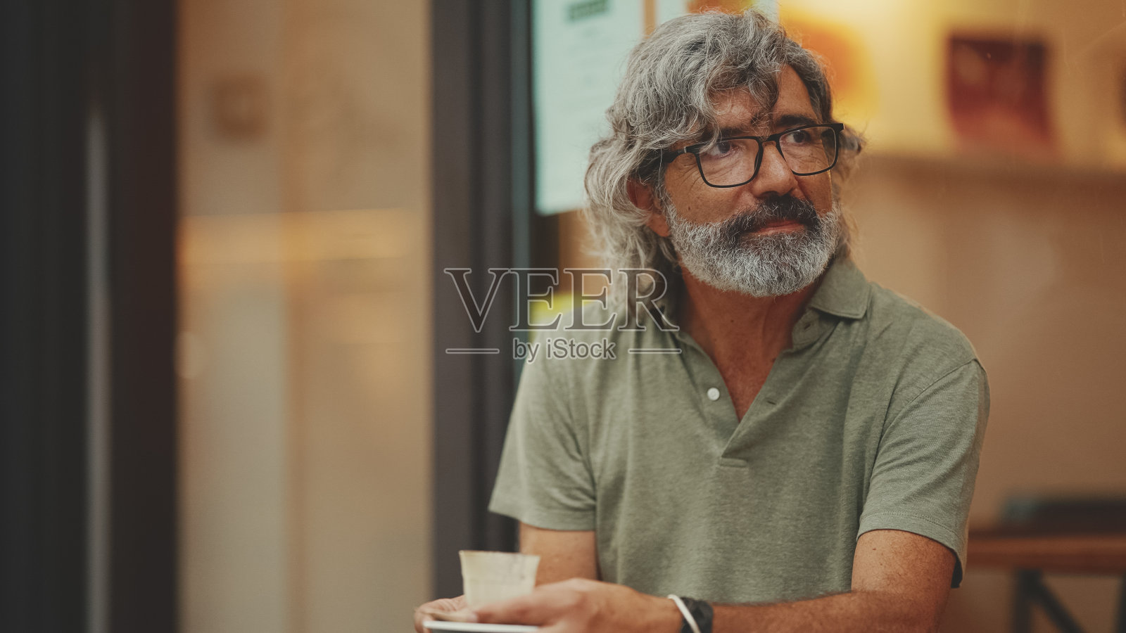 阴沉的，沉思的中年男子，灰白的头发和胡子，穿着便服，坐在街上的咖啡馆。戴眼镜的成熟绅士喝香气咖啡照片摄影图片