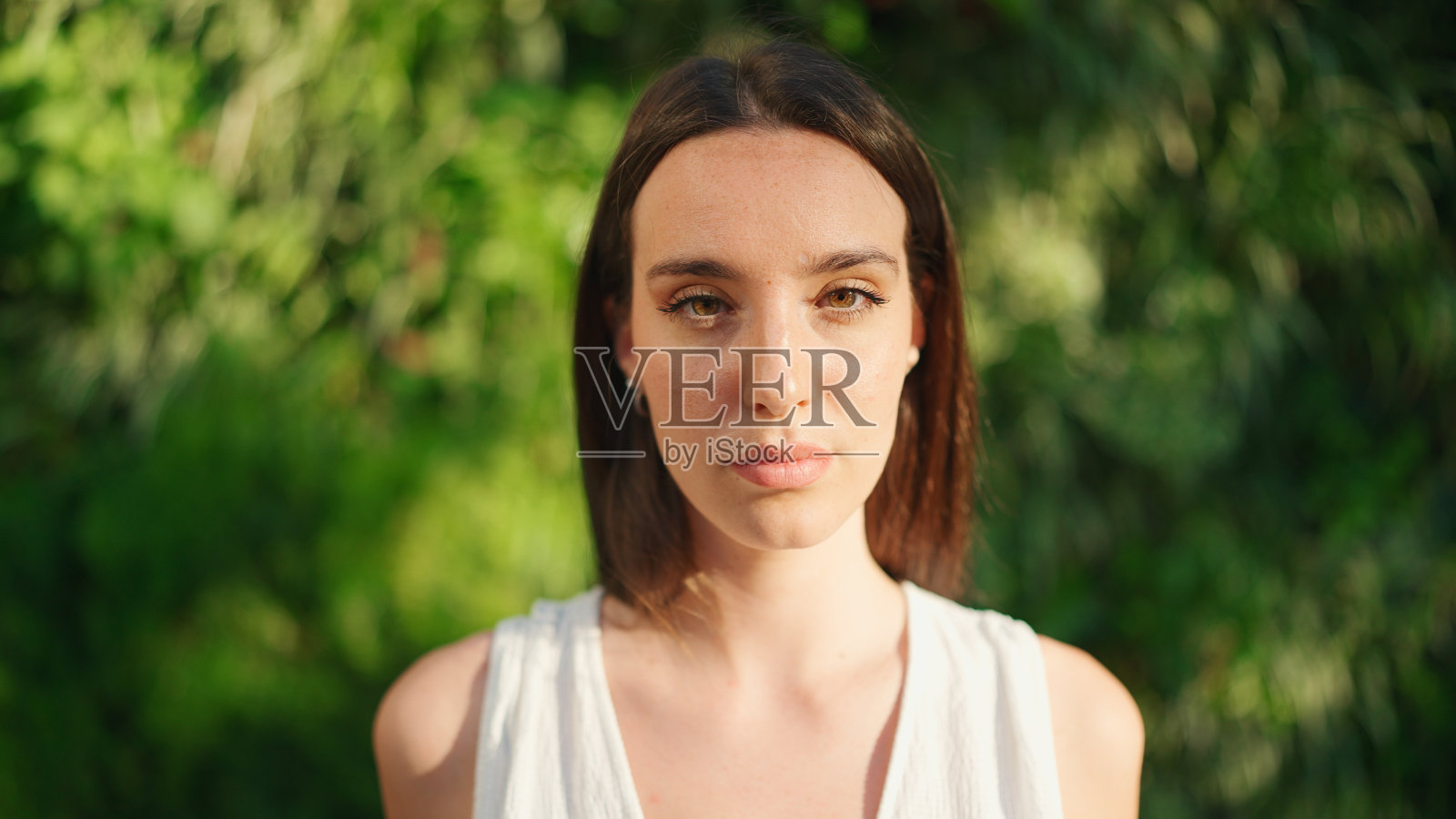 年轻女子的肖像与雀斑和黑色松散的头发穿着白色上衣和牛仔裤看着相机照片摄影图片