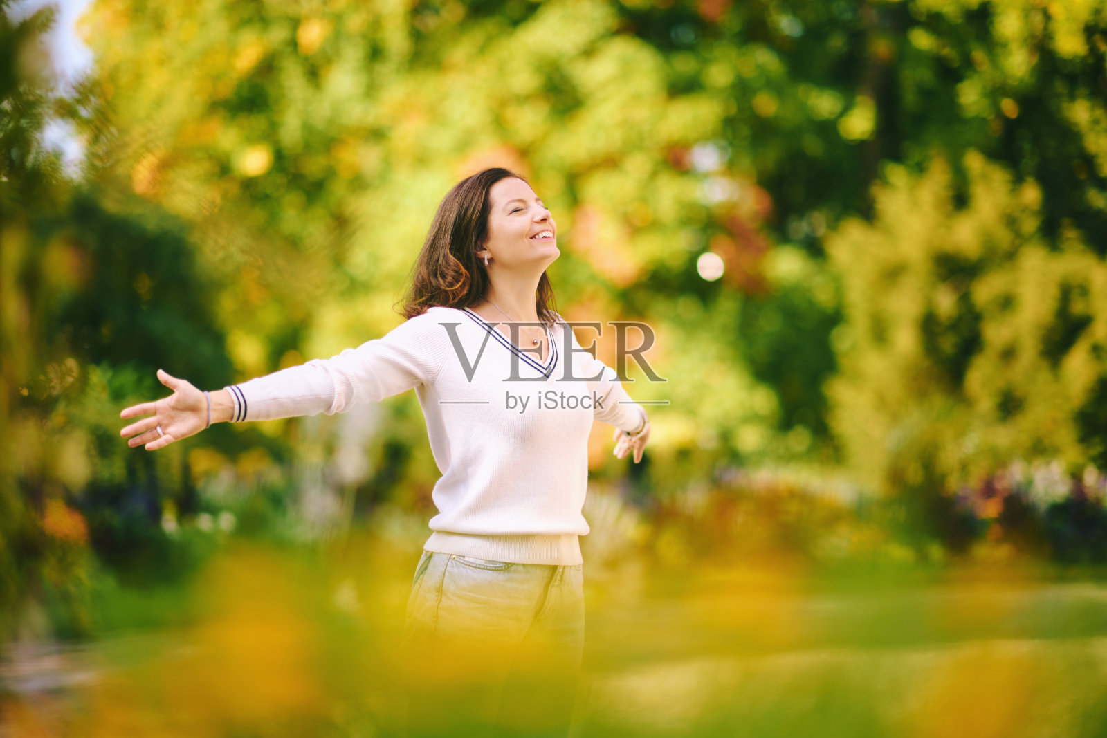 户外肖像快乐和健康的40 - 45岁的妇女在公园享受美好的阳光，双臂张开照片摄影图片