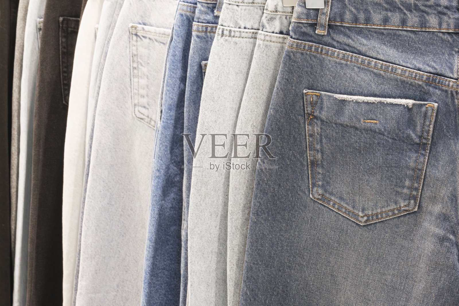 许多牛仔裤挂在衣架上。一排裤子牛仔牛仔裤挂在衣柜里，买，卖，购物和牛仔裤时尚的概念照片摄影图片