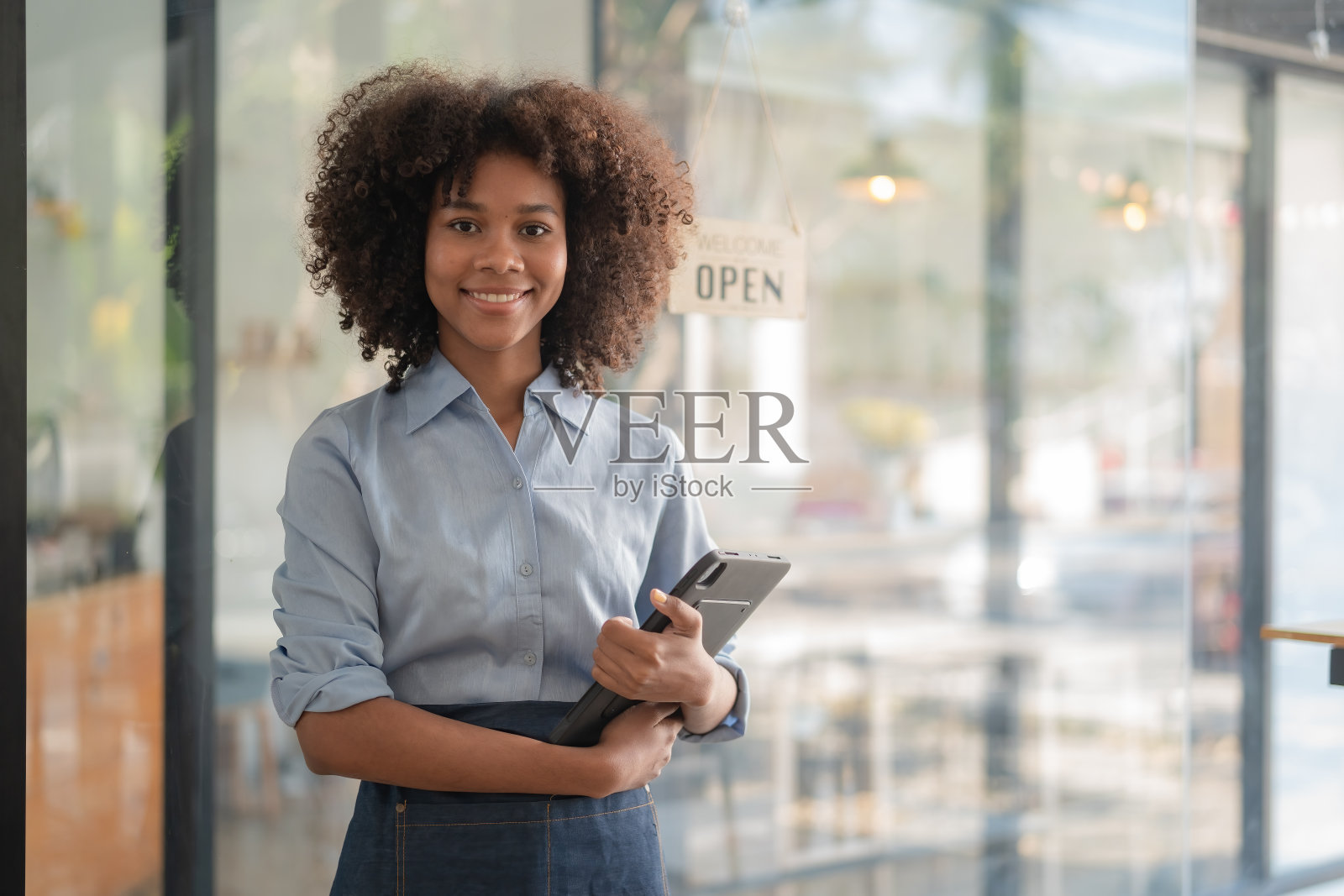 在咖啡店吧台前，一名年轻的非裔美国女性正在创业，她系着围裙，露出笑容。照片摄影图片