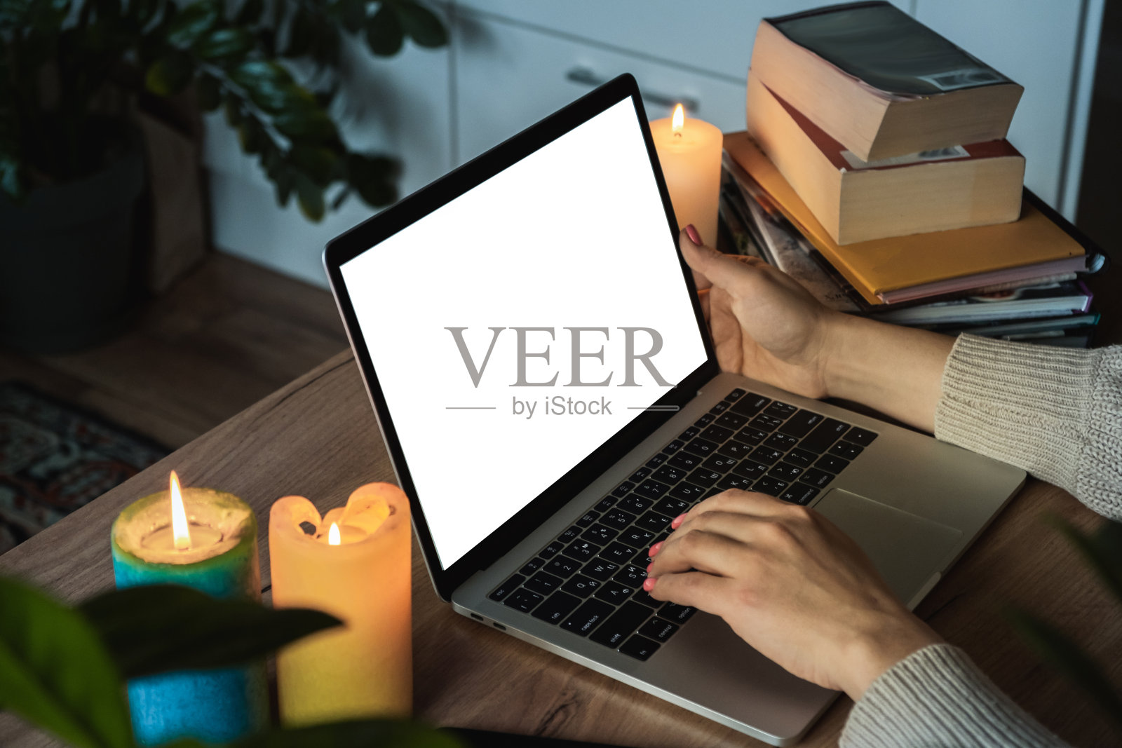 在停电期间，女人用手在笔记本电脑键盘上打字的特写。在电脑前用白屏工作，在停电时点上蜡烛。能源危机概念的模型照片摄影图片