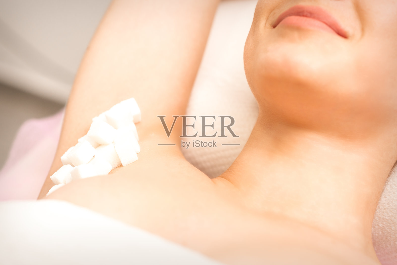 上糖，打蜡的概念。白糖方块躺在年轻白女的腋下，靠近。照片摄影图片