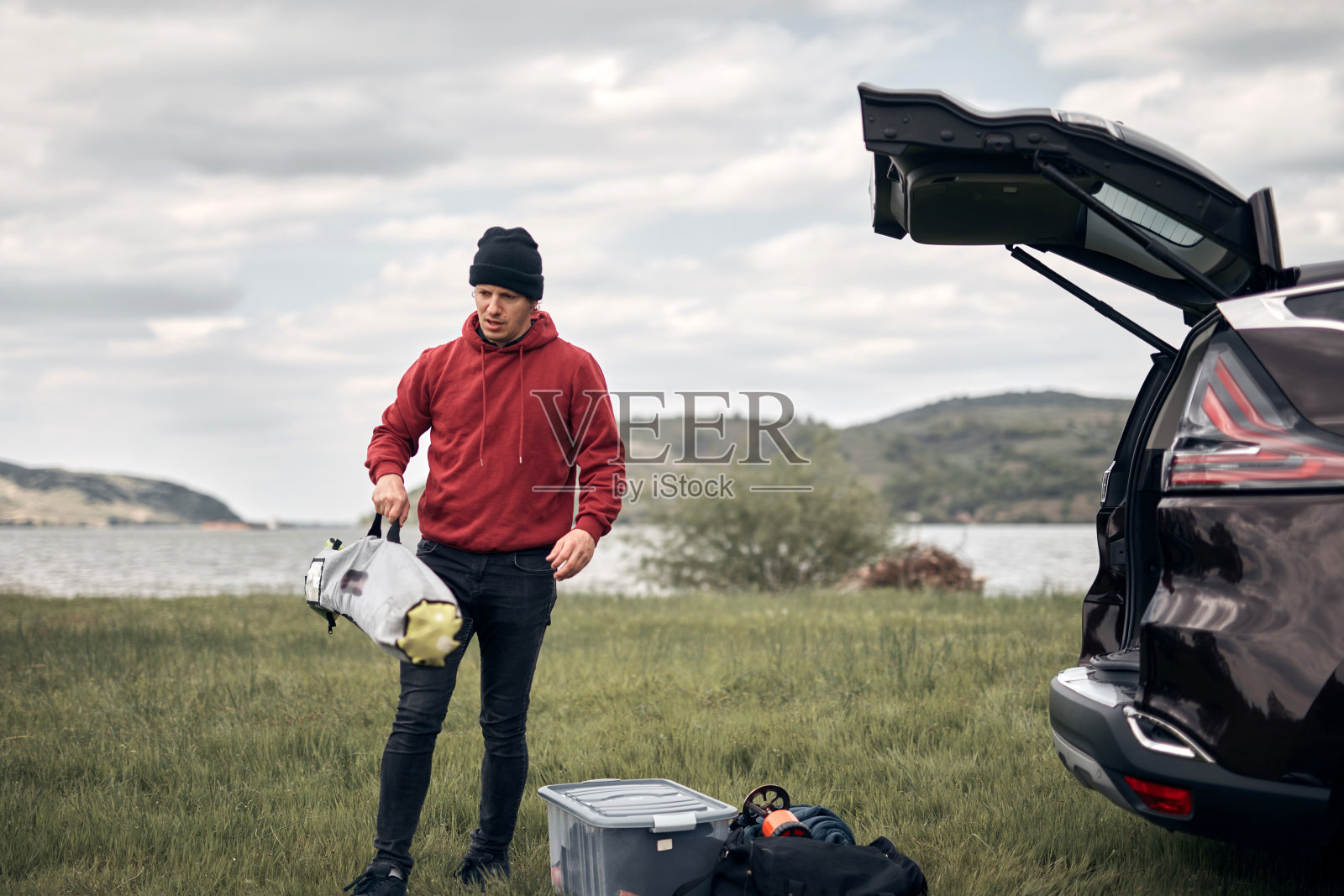 风帆冲浪者和露营者在湖边附近的大自然中从车上卸下设备。照片摄影图片