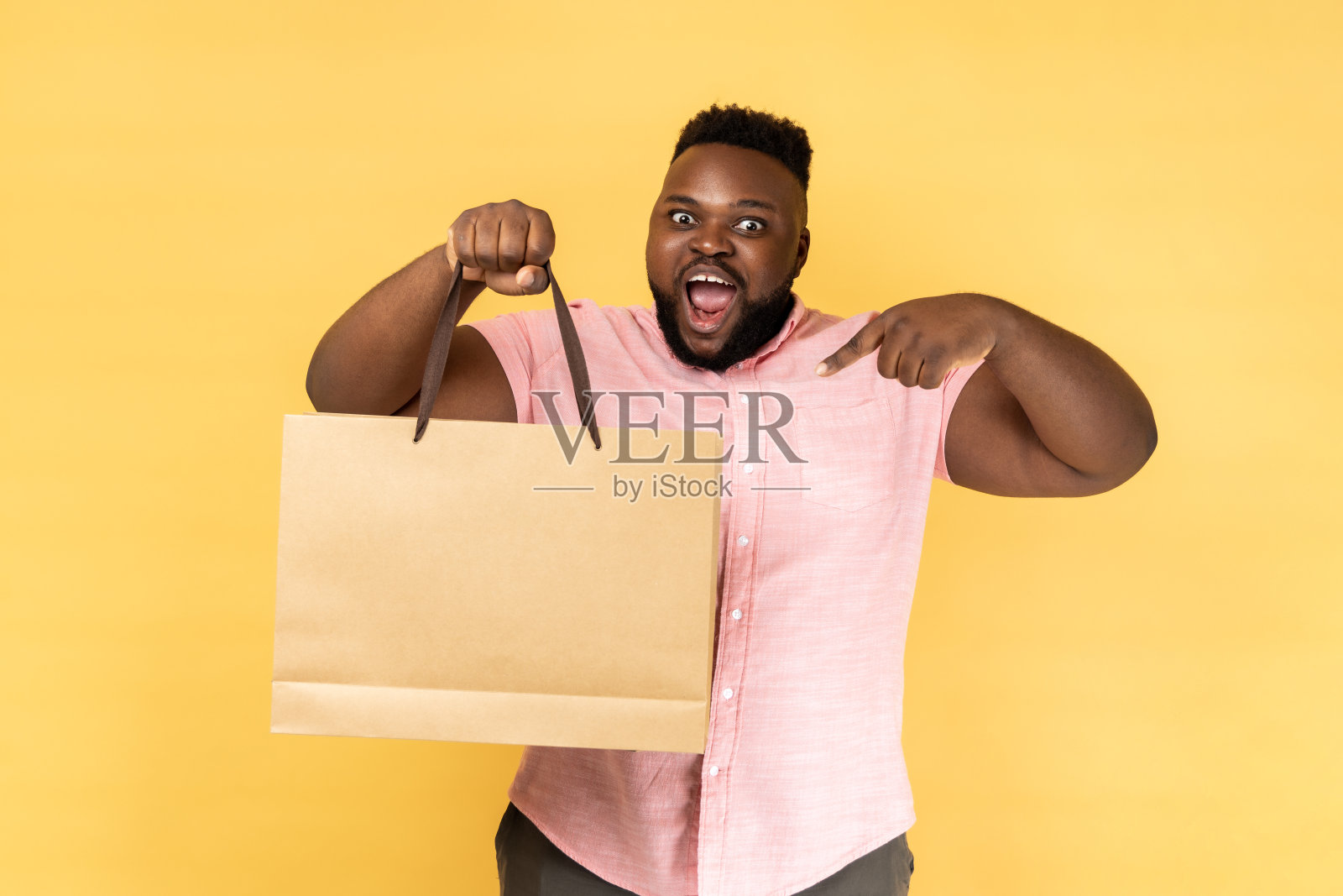 男子指着购物袋，看着镜头，脸上露出高兴的表情。照片摄影图片