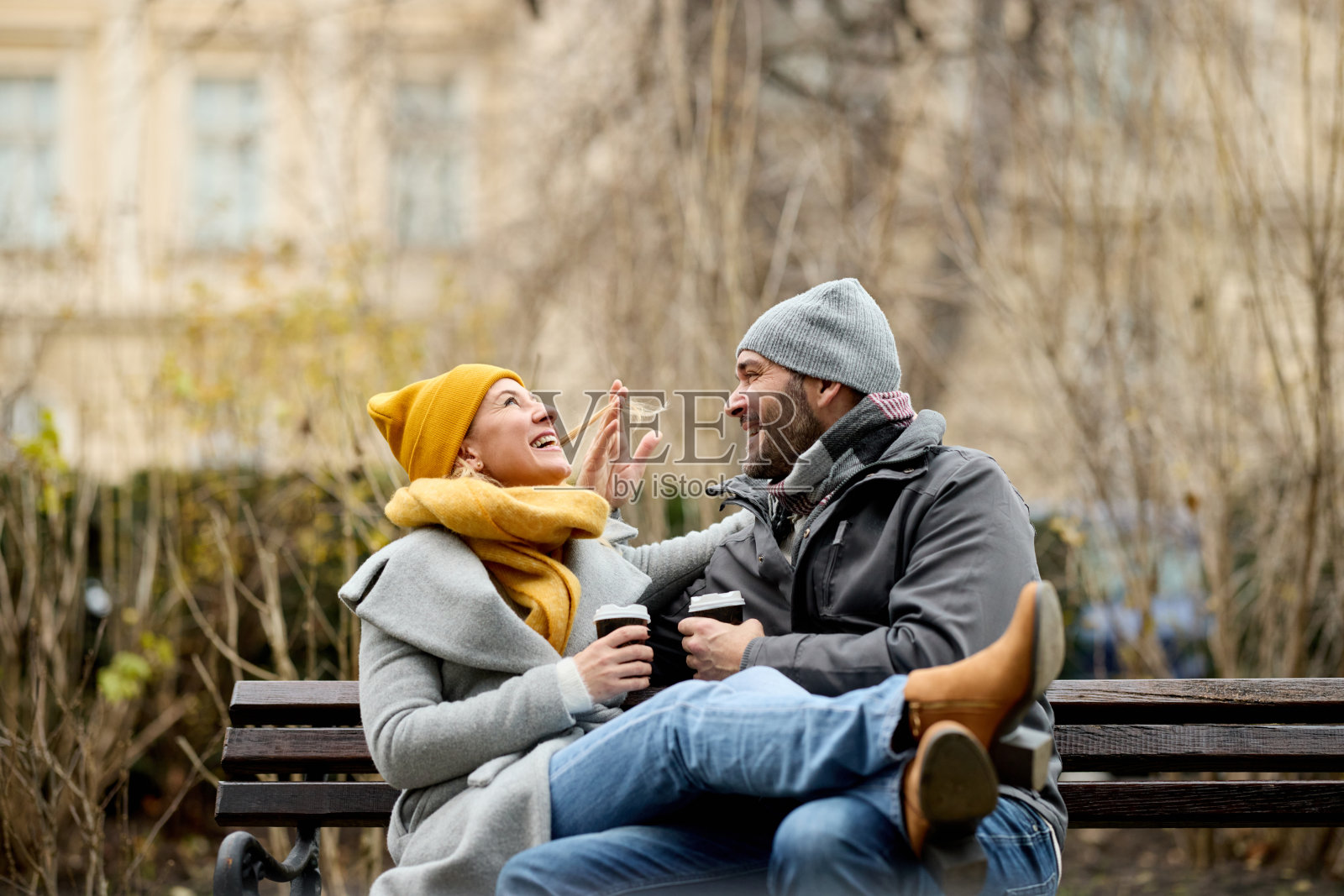 冬天的户外，一对情侣坐在公园长椅上喝热饮照片摄影图片