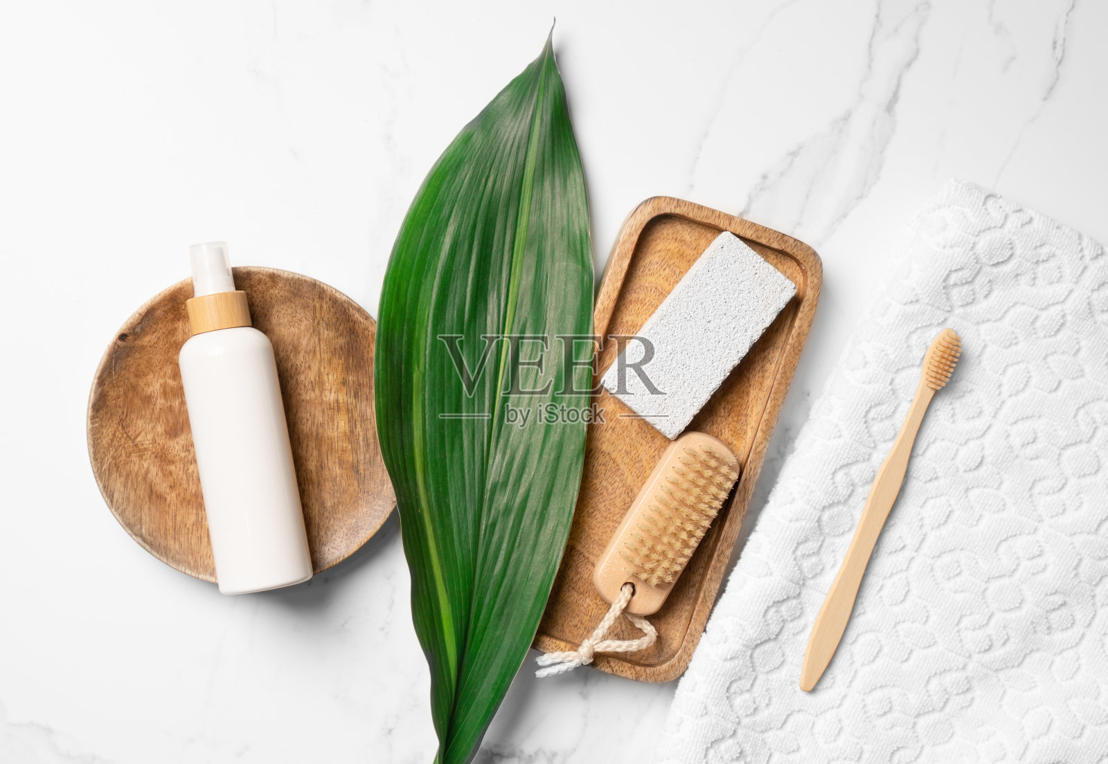 身体护理必需品包括牙刷、白色毛巾、浮石、刷子、绿叶和白色化妆品瓶子模型。照片摄影图片