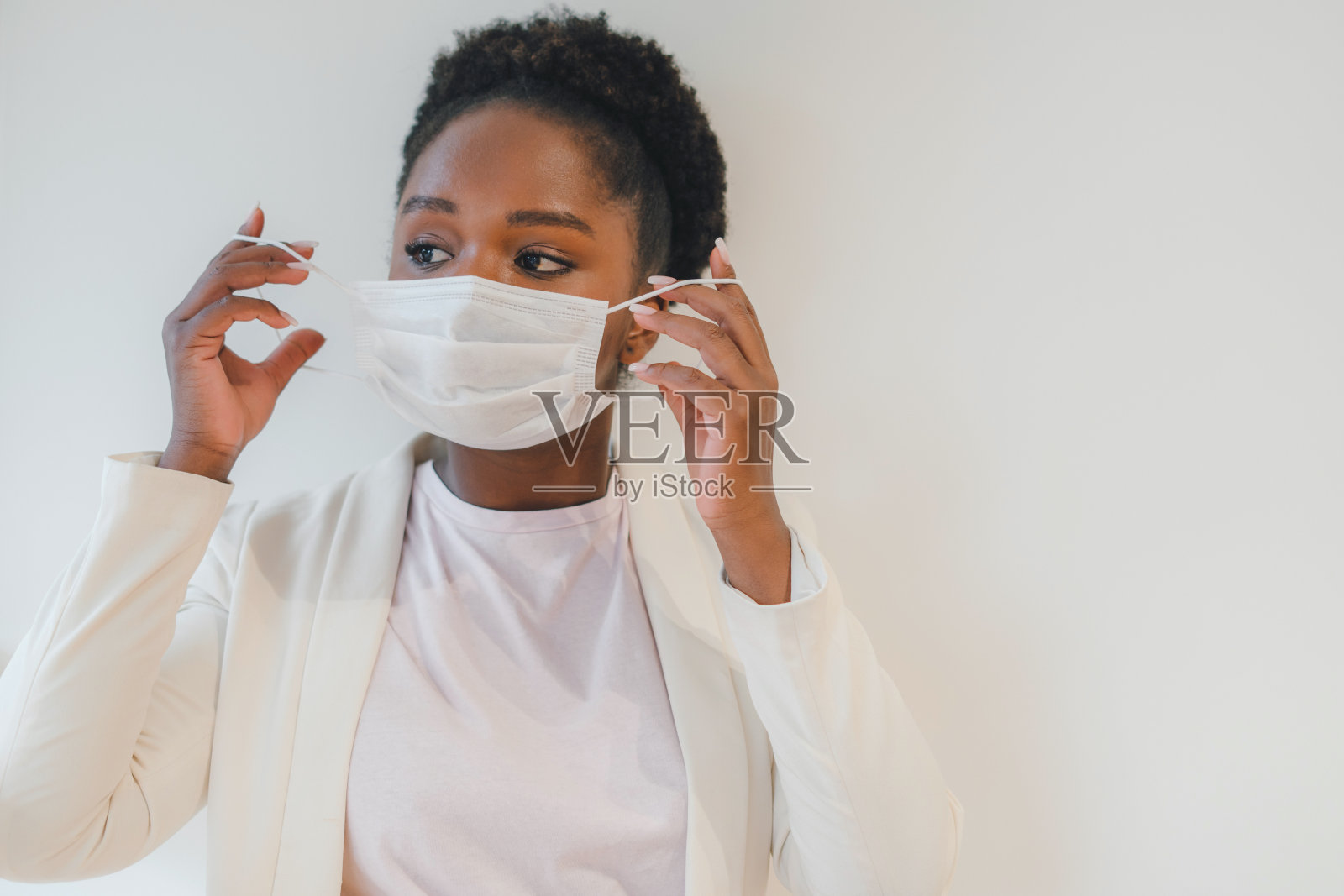 一名身穿白色夹克、戴着医用口罩的非裔美国妇女的肖像，她的目光被隔离在墙上。自我隔离，预防，隔离，covid - 19，冠状病毒概念照片摄影图片