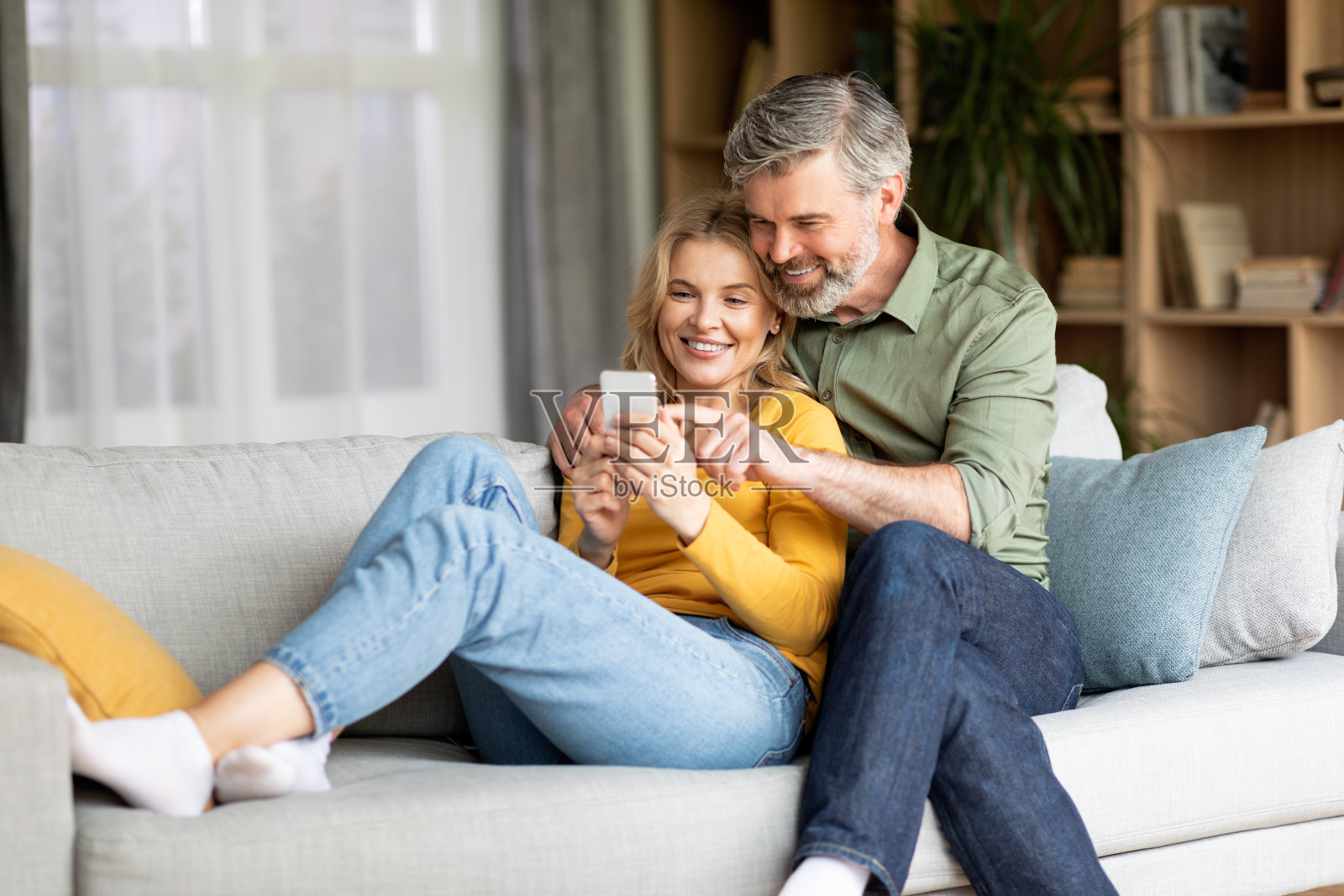 美丽的中年夫妇在家里用手机拥抱在一起照片摄影图片