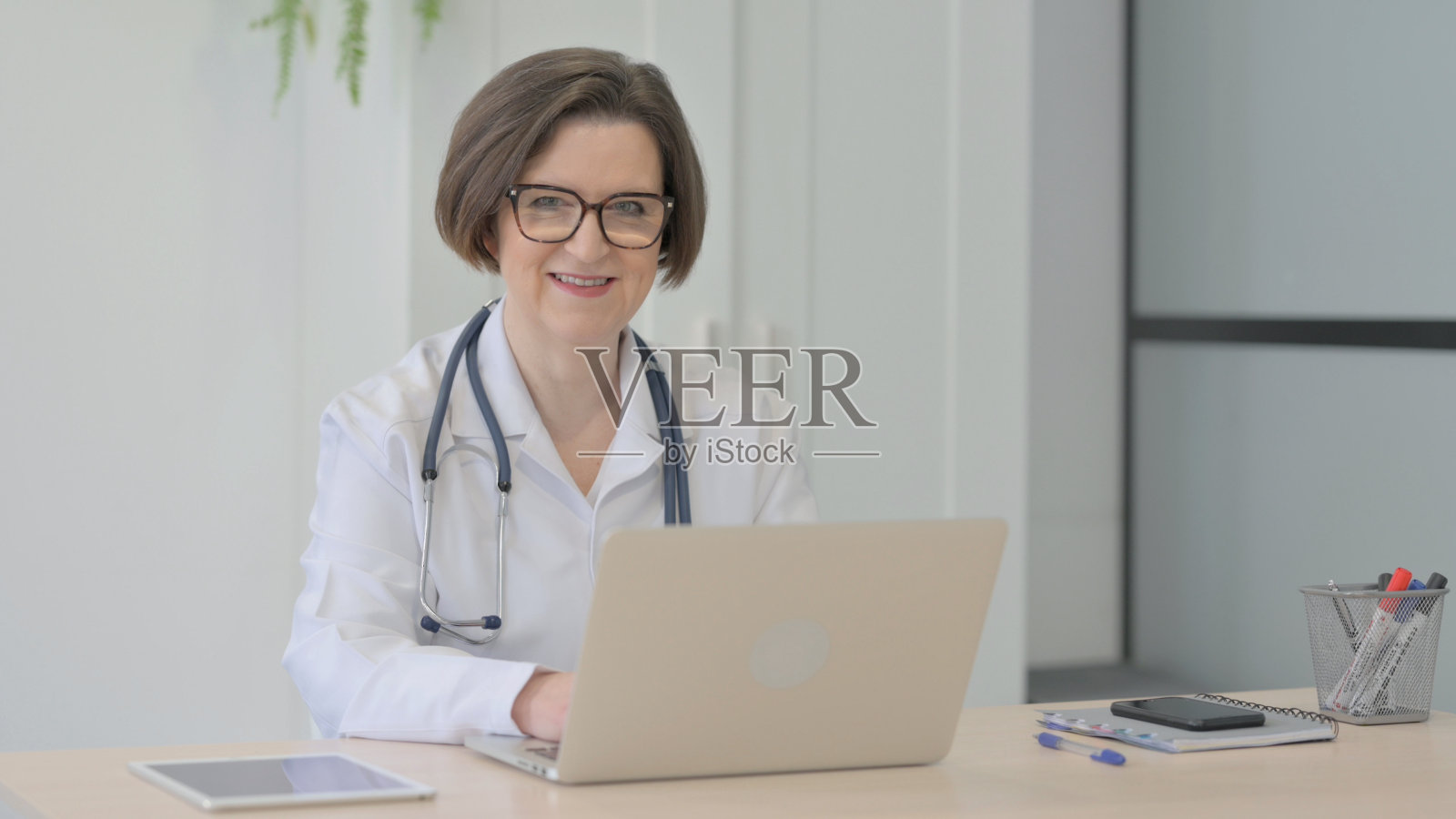 老女医生在使用笔记本电脑时对着相机微笑照片摄影图片