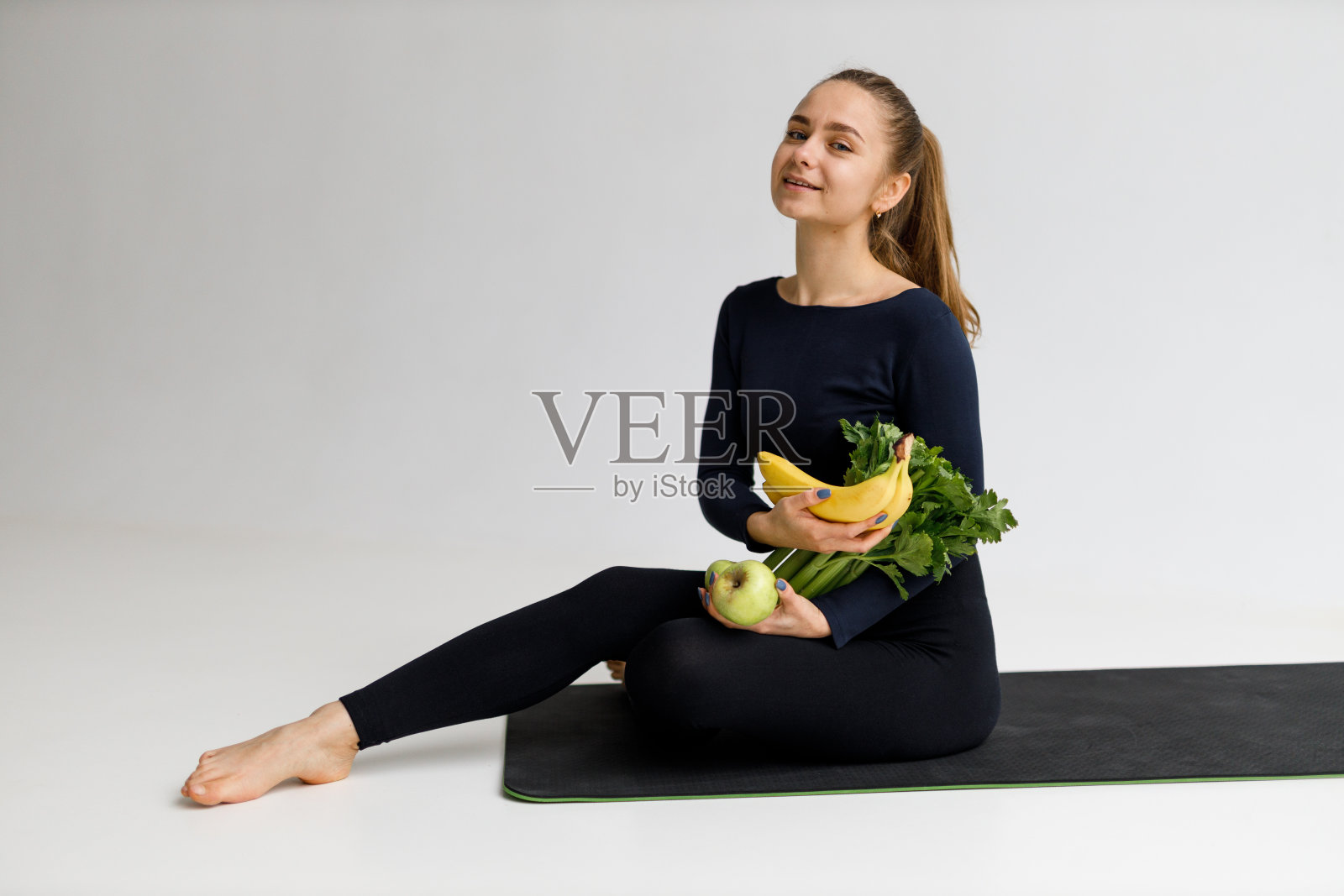 一个穿着运动服的成年素食妇女的肖像，她手里拿着水果和蔬菜，白色背景。照片摄影图片