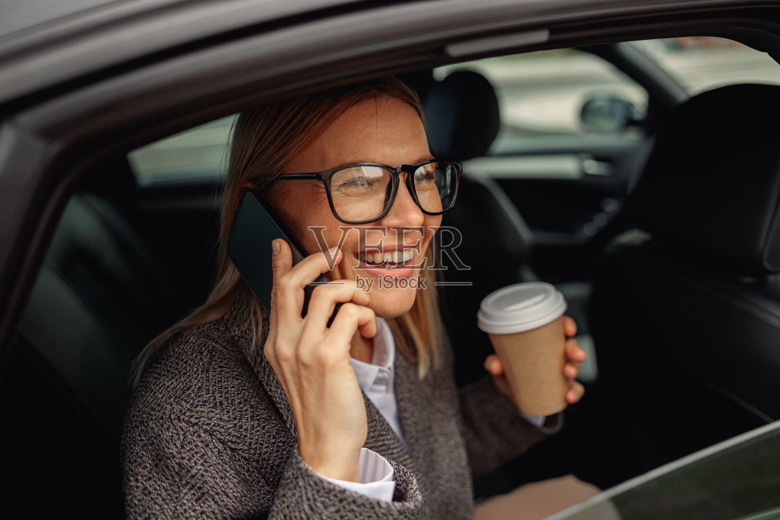 女人拿着咖啡，坐在出租车后座上打电话，在上班的路上看着窗户照片摄影图片
