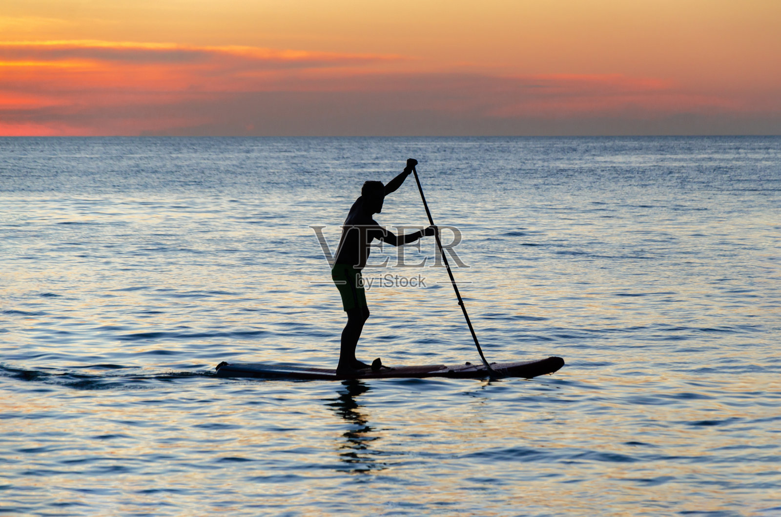 男人的剪影是划船在一个SUP板对日落天空的背景。站paddleboarding照片摄影图片