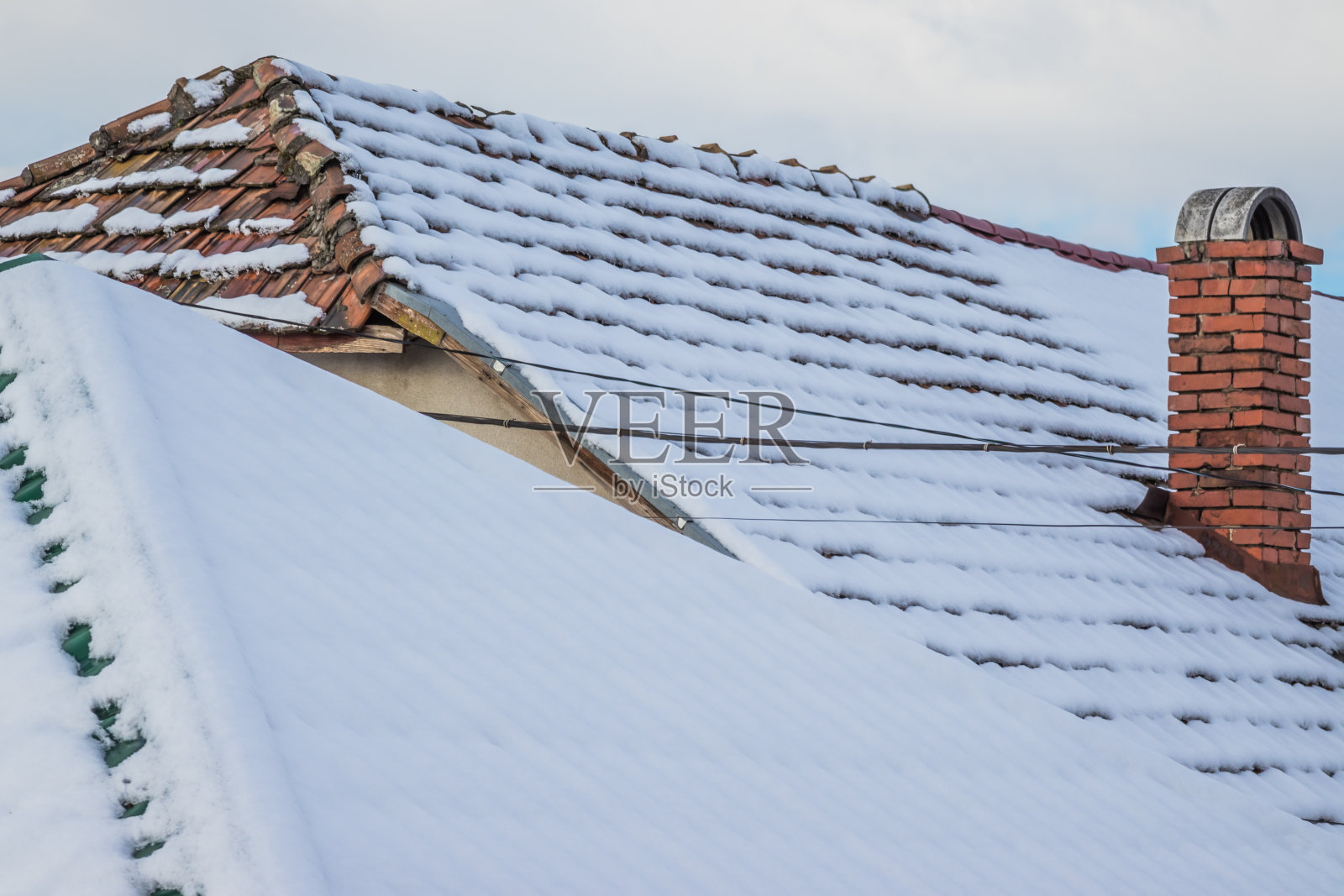 雪中一座私人住宅的屋顶。雪中的瓦片屋顶。冬天的时间。屋顶被雪覆盖着。部分屋顶没有积雪。照片摄影图片