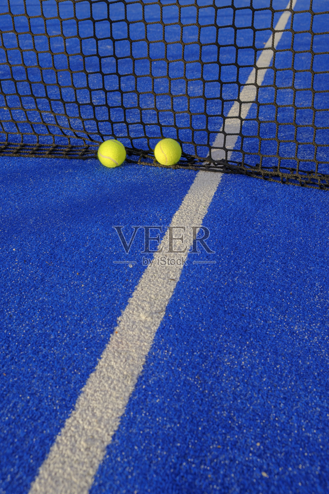 蓝桨网球场网旁的两个球。照片摄影图片